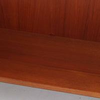 Nils JonssonがTroeds社のためにデザインした「Domi Monté」モデルのディスプレイシェルフ。チーク材を贅沢に使用し、温かみのある木肌と洗練されたフォルムが魅力の一台です。上部には高さ調整が可能な可動棚が8枚備わり、本やオブジェのディスプレイに柔軟に対応。下部には扉付き収納と仕切り付きの引き出しが配されており、実用性にも優れます。背面にはTroeds社の刻印が残されており、スウェーデン製ビンテージ家具としての確かな出自を物語ります。空間に落ち着きと上質な雰囲気を添える、北欧モダンらしい逸品です。