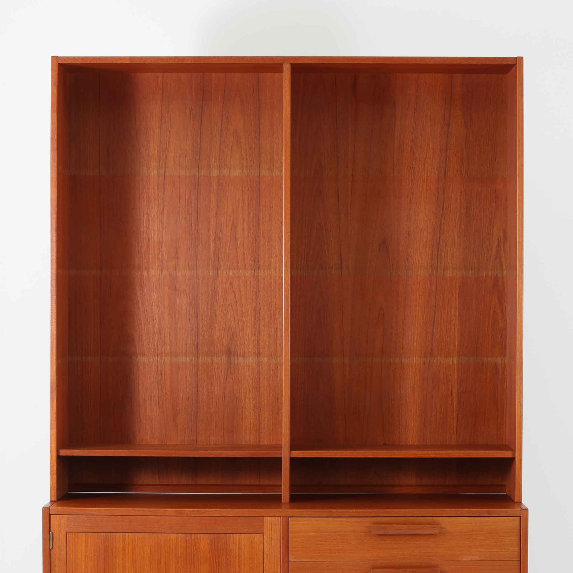 Nils JonssonがTroeds社のためにデザインした「Domi Monté」モデルのディスプレイシェルフ。チーク材を贅沢に使用し、温かみのある木肌と洗練されたフォルムが魅力の一台です。上部には高さ調整が可能な可動棚が8枚備わり、本やオブジェのディスプレイに柔軟に対応。下部には扉付き収納と仕切り付きの引き出しが配されており、実用性にも優れます。背面にはTroeds社の刻印が残されており、スウェーデン製ビンテージ家具としての確かな出自を物語ります。空間に落ち着きと上質な雰囲気を添える、北欧モダンらしい逸品です。