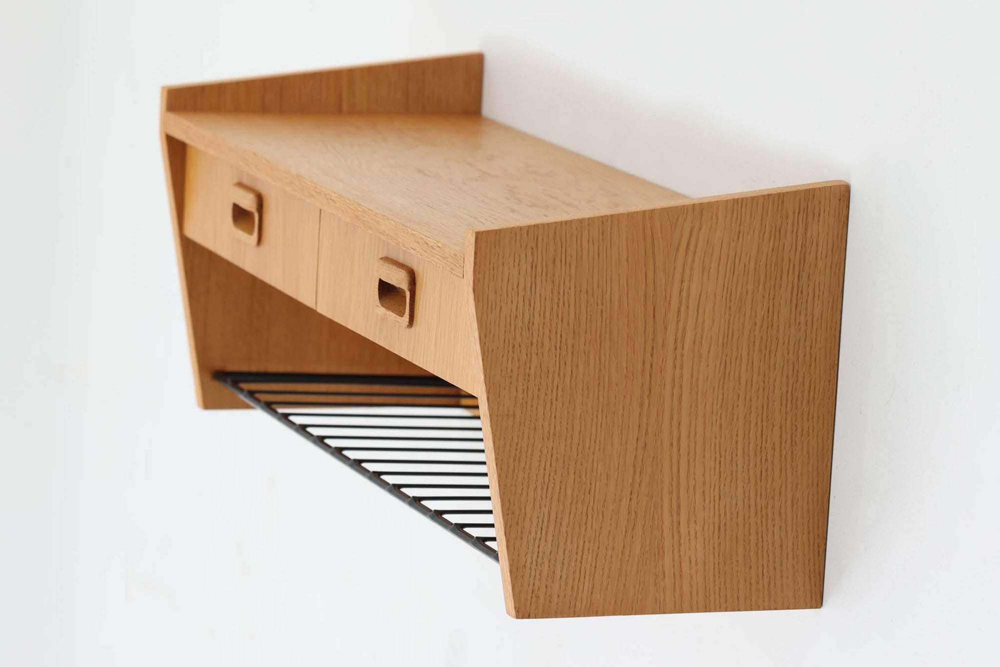 スウェーデン製のヴィンテージウォールシェルフ。素材には木目の美しいオーク材を使用し、下部にはスチール製のバーがあしらわれた、実用性とデザイン性を兼ね備えた一台です。緩やかに角度のついたサイドパネルが印象的で、北欧らしいモダンな佇まいを見せてくれます。2杯の引き出しは小物収納に便利で、下段のバーにはストールや雑誌などを置く事も可能。玄関やリビング、キッチンなどさまざまな空間で活躍する、機能的で美しいウォールシェルフです。