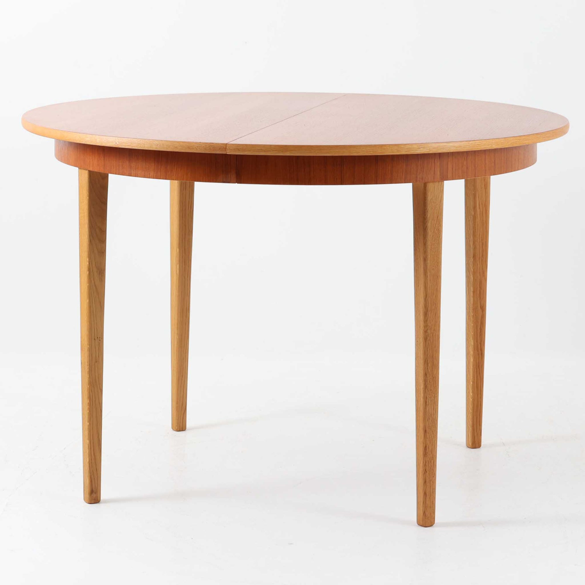 チーク材の天板とオーク材の脚部が美しく調和したこちらの円形エクステンションダイニングテーブルは、デンマーク製ならではの丁寧な仕上げと実用性が魅力の北欧ビンテージ家具です。直径110cmの円形天板は、中央に拡張板を2枚追加することで広々としたオーバル型に変化し、来客時やホームパーティーなどにも柔軟に対応できます。細身のテーパー脚が軽やかな印象を与え、温かみのある木の表情が空間に自然と溶け込む逸品です。