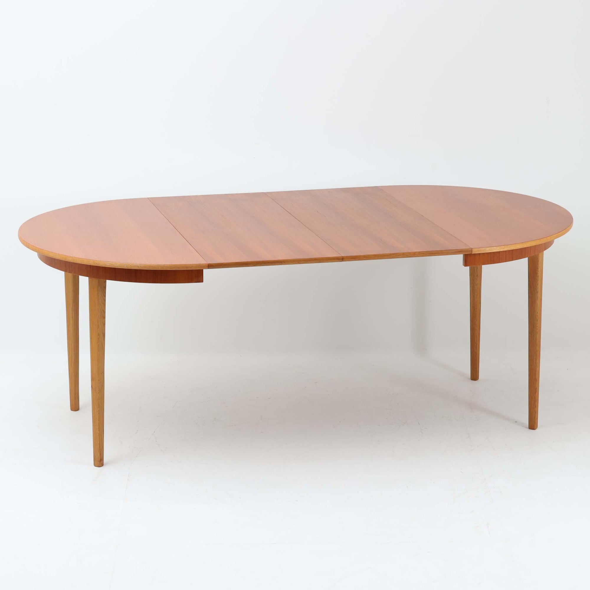 チーク材の天板とオーク材の脚部が美しく調和したこちらの円形エクステンションダイニングテーブルは、デンマーク製ならではの丁寧な仕上げと実用性が魅力の北欧ビンテージ家具です。直径110cmの円形天板は、中央に拡張板を2枚追加することで広々としたオーバル型に変化し、来客時やホームパーティーなどにも柔軟に対応できます。細身のテーパー脚が軽やかな印象を与え、温かみのある木の表情が空間に自然と溶け込む逸品です。