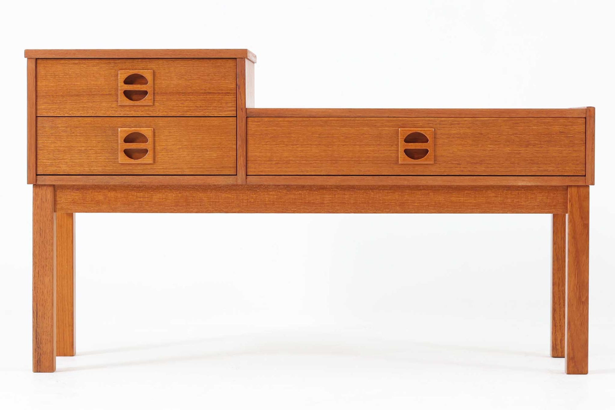 スウェーデン製のミッドセンチュリーモダンスタイル。チーク材を贅沢に使用し、北欧デザインらしい洗練されたフォルムと機能性を兼ね備えています。特徴的な段差のあるデザインで、左側に2段、右側に1段の引き出しを配置。半円形の木製取っ手がアクセントになっています。コンパクトなサイズで、電話台やサイドテーブルとして玄関やリビングなど幅広く活躍。引き出しは小物や書類の収納に便利で、天板には観葉植物や写真立てを飾るのに最適です。チーク材ならではの温かみと美しい木目が、ヴィンテージならではの魅力を引き立てます。