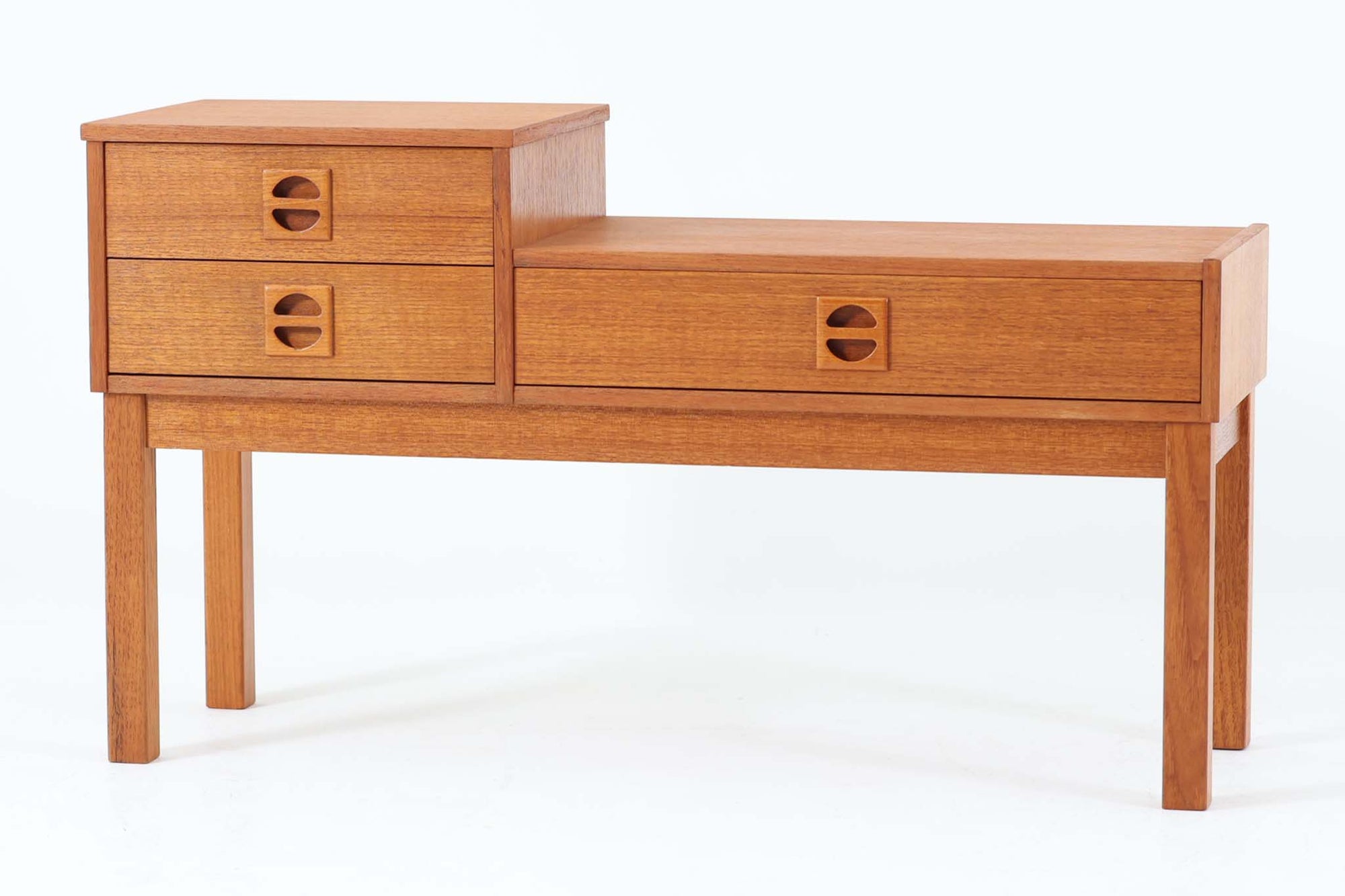 スウェーデン製のミッドセンチュリーモダンスタイル。チーク材を贅沢に使用し、北欧デザインらしい洗練されたフォルムと機能性を兼ね備えています。特徴的な段差のあるデザインで、左側に2段、右側に1段の引き出しを配置。半円形の木製取っ手がアクセントになっています。コンパクトなサイズで、電話台やサイドテーブルとして玄関やリビングなど幅広く活躍。引き出しは小物や書類の収納に便利で、天板には観葉植物や写真立てを飾るのに最適です。チーク材ならではの温かみと美しい木目が、ヴィンテージならではの魅力を引き立てます。