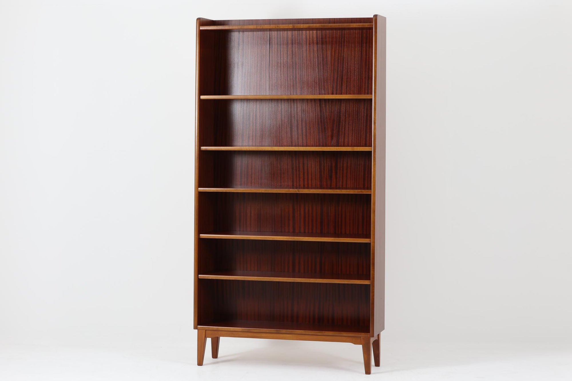 スウェーデンで製造されたヴィンテージのブックシェルフ。本体には深みのある美しいマホガニー材を使用し、縁や脚部にはナチュラルな風合いのビーチ材を組み合わせた、上品で洗練されたデザインが魅力です。特徴的なのは、上から下に向かって奥行が深くなる構造。視覚的な軽やかさを保ちながらも収納力を確保し、機能性とデザイン性を両立した作りになっています。脚部の緩やかな曲線が北欧家具らしいエレガントな印象を与え、インテリアに品のある温かみをプラスしてくれます。書籍やディスプレイアイテムを美しく収納できる、実用性とデザイン性を兼ね備えた一品。シンプルながらもこだわりを感じさせる北欧ヴィンテージ家具をお探しの方におすすめです。