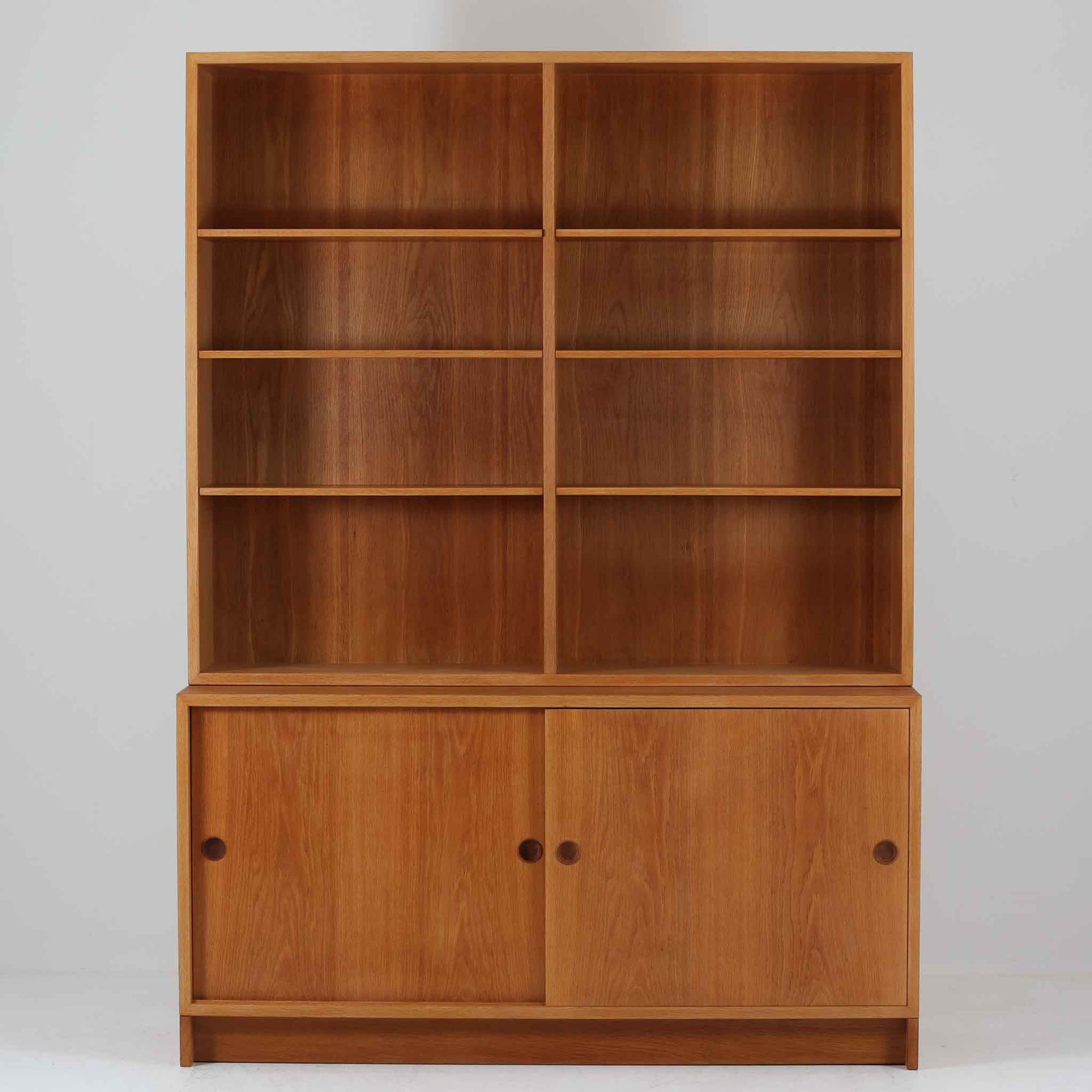 スウェーデンのKarl Andersson社より、Borge Mogensenによってデザインされたディスプレイシェルフは、端正な佇まいと機能性を兼ね備えた北欧ビンテージ家具です。オーク材の温もりある質感と美しい木目が魅力で、上段は可動棚付きのオープンシェルフ、下段には丸い掘り込み取手がアクセントとなった引き戸収納が配されています。文庫本や器、日用品の整理に最適で、暮らしの中で永く使い続けられる名作です。