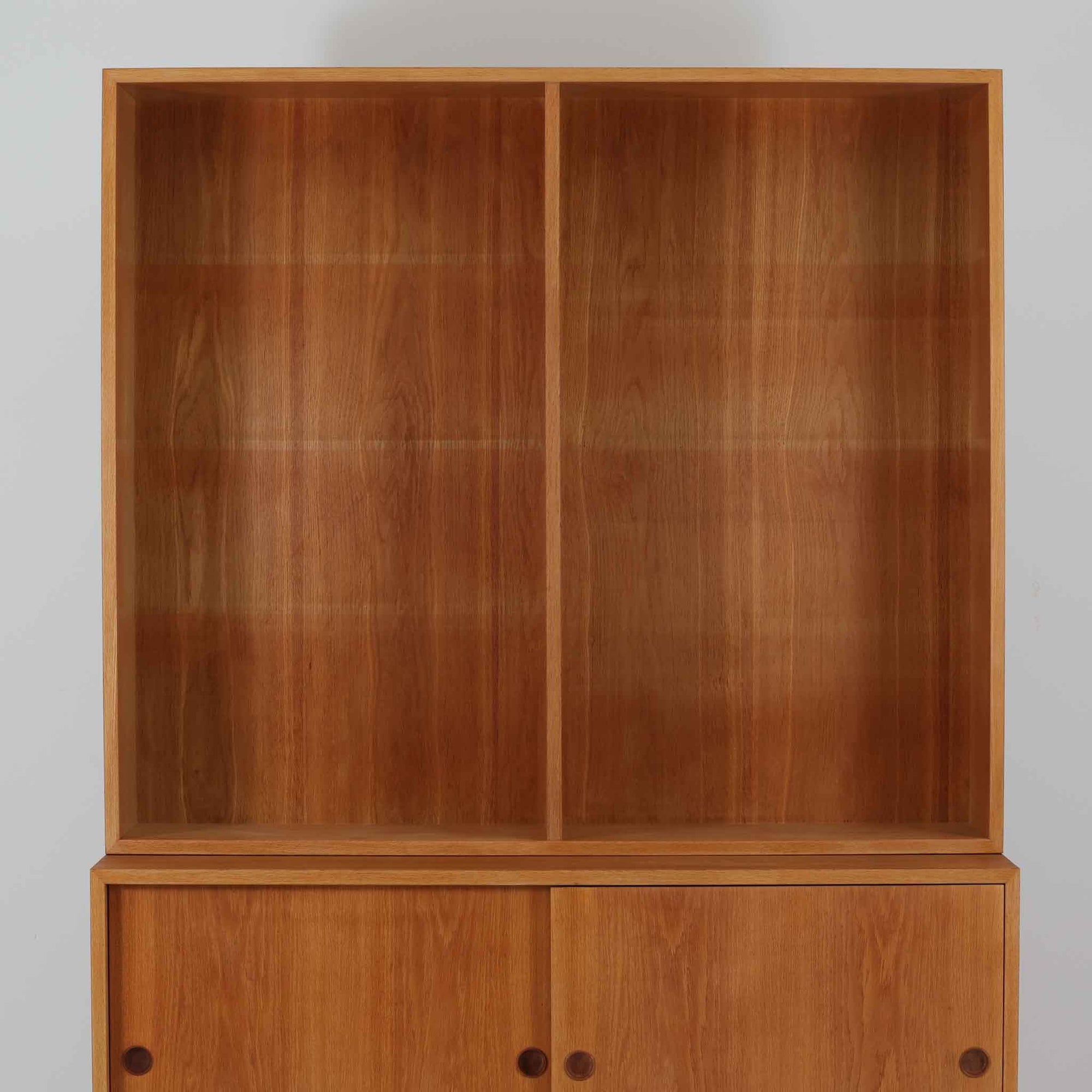 スウェーデンのKarl Andersson社より、Borge Mogensenによってデザインされたディスプレイシェルフは、端正な佇まいと機能性を兼ね備えた北欧ビンテージ家具です。オーク材の温もりある質感と美しい木目が魅力で、上段は可動棚付きのオープンシェルフ、下段には丸い掘り込み取手がアクセントとなった引き戸収納が配されています。文庫本や器、日用品の整理に最適で、暮らしの中で永く使い続けられる名作です。