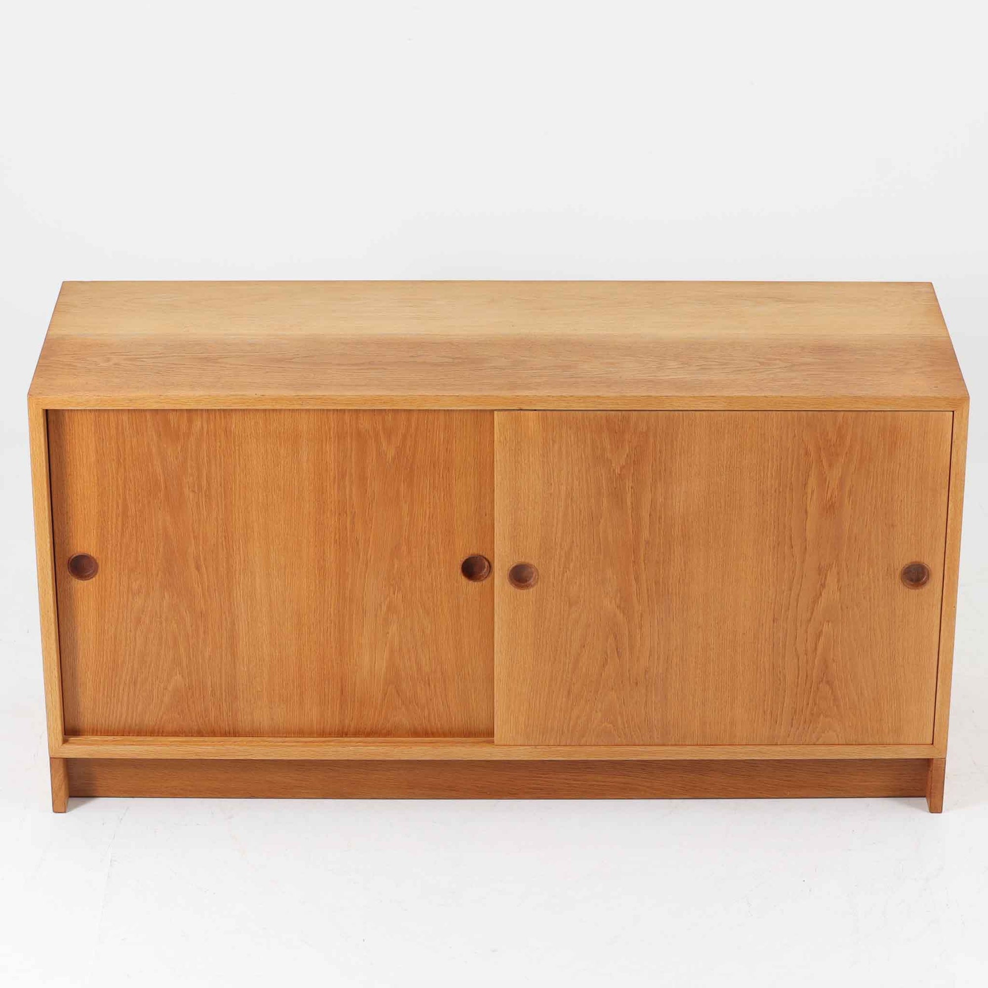 スウェーデンのKarl Andersson社より、Borge Mogensenによってデザインされたディスプレイシェルフは、端正な佇まいと機能性を兼ね備えた北欧ビンテージ家具です。オーク材の温もりある質感と美しい木目が魅力で、上段は可動棚付きのオープンシェルフ、下段には丸い掘り込み取手がアクセントとなった引き戸収納が配されています。文庫本や器、日用品の整理に最適で、暮らしの中で永く使い続けられる名作です。