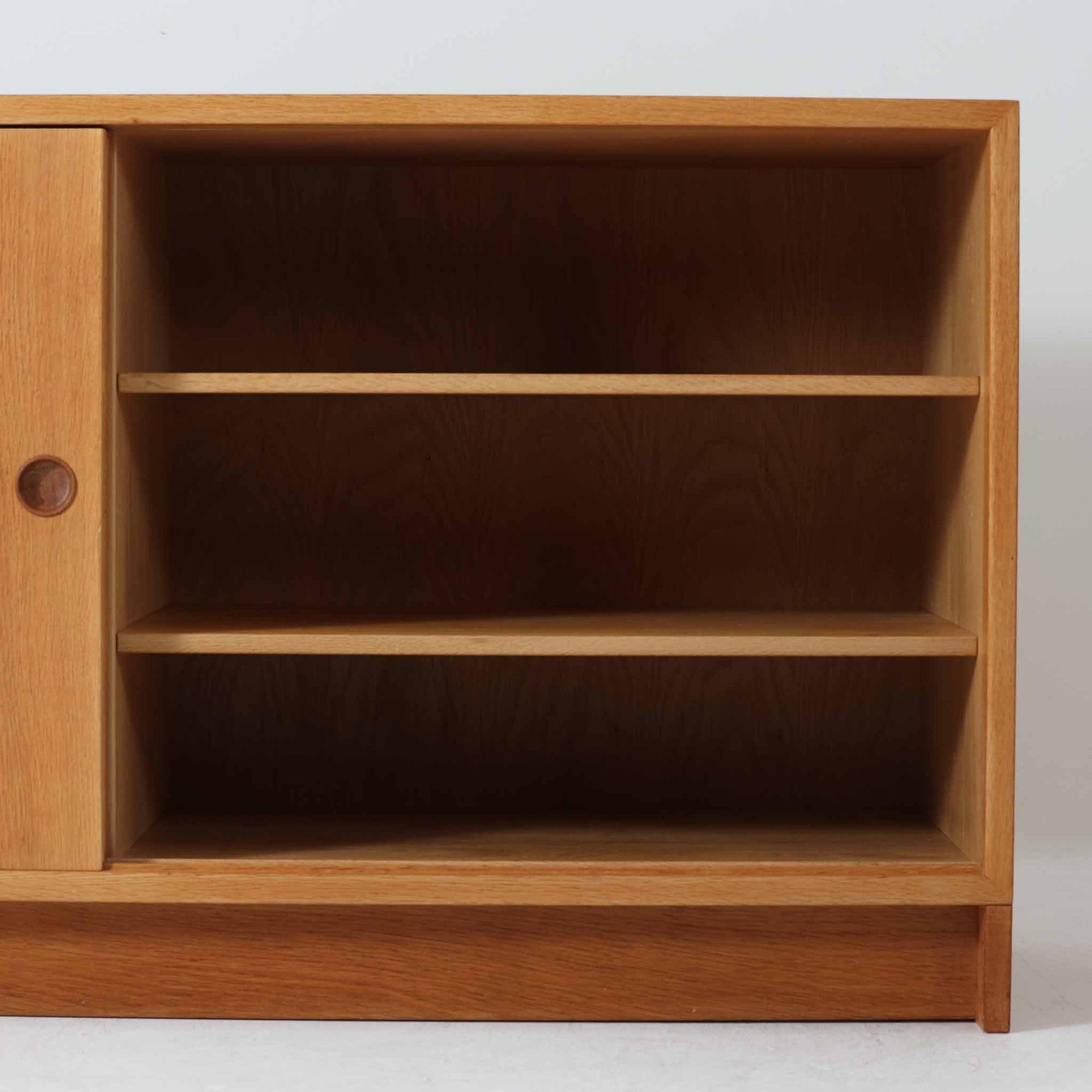 スウェーデンのKarl Andersson社より、Borge Mogensenによってデザインされたディスプレイシェルフは、端正な佇まいと機能性を兼ね備えた北欧ビンテージ家具です。オーク材の温もりある質感と美しい木目が魅力で、上段は可動棚付きのオープンシェルフ、下段には丸い掘り込み取手がアクセントとなった引き戸収納が配されています。文庫本や器、日用品の整理に最適で、暮らしの中で永く使い続けられる名作です。