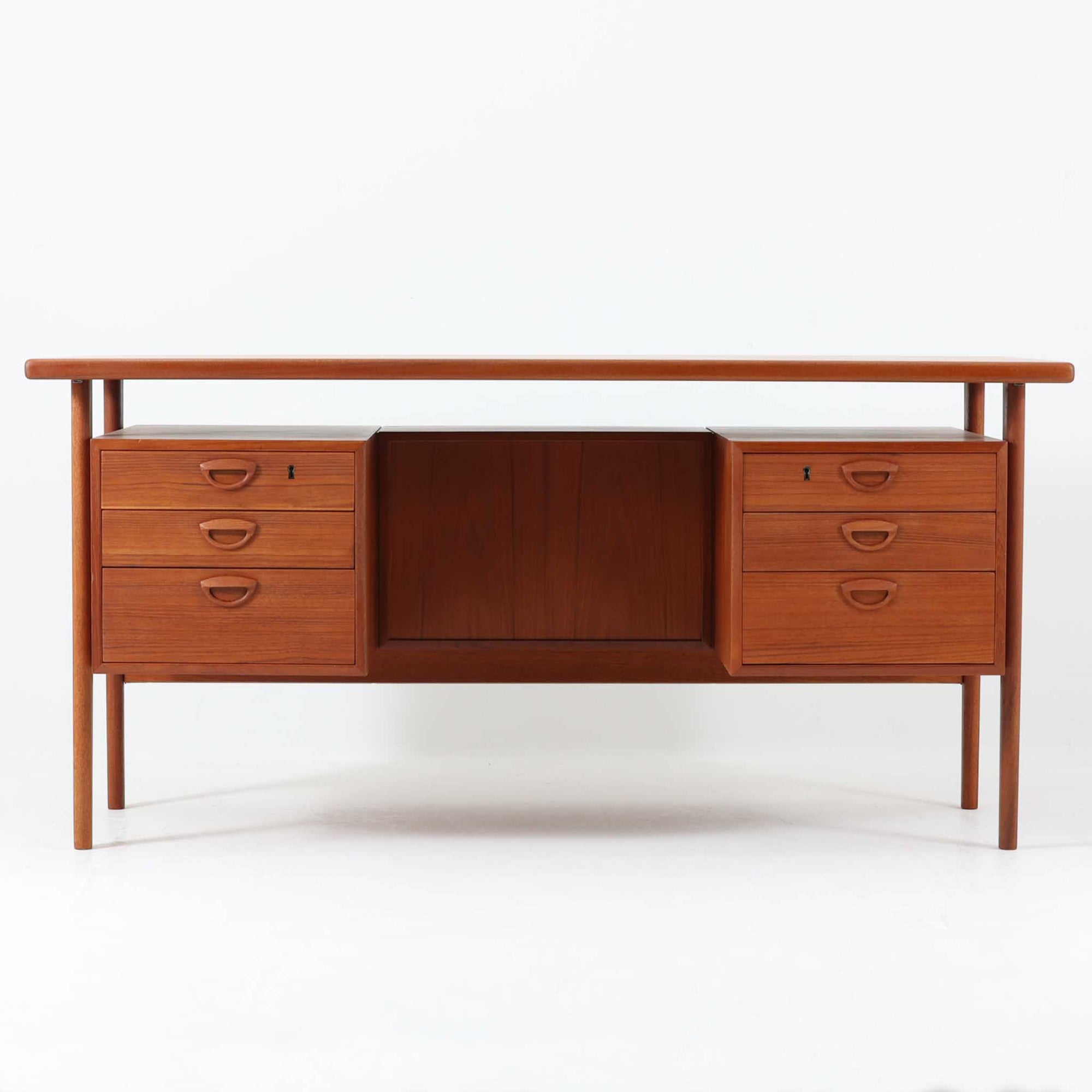 カイ・クリスチャンセンがデザインし、FM furniture社によって製造されたこちらの両袖デスクは、チーク材の美しい木目と温かみのある色合いが魅力の北欧ビンテージ家具です。左右には3杯ずつの引き出し、中央には扉付き収納を備え、背面にはオープンシェルフが設けられており、デスクとしての高い収納力と機能性を誇ります。壁付けはもちろん、間仕切りとしても活用できるため、空間の中心にも映える設計です。丸みを帯びた取手や脚部など、細部にまでこだわった意匠は、カイ・クリスチャンセンらしい洗練された美しさを体現しており、上質なワークスペースを演出します。