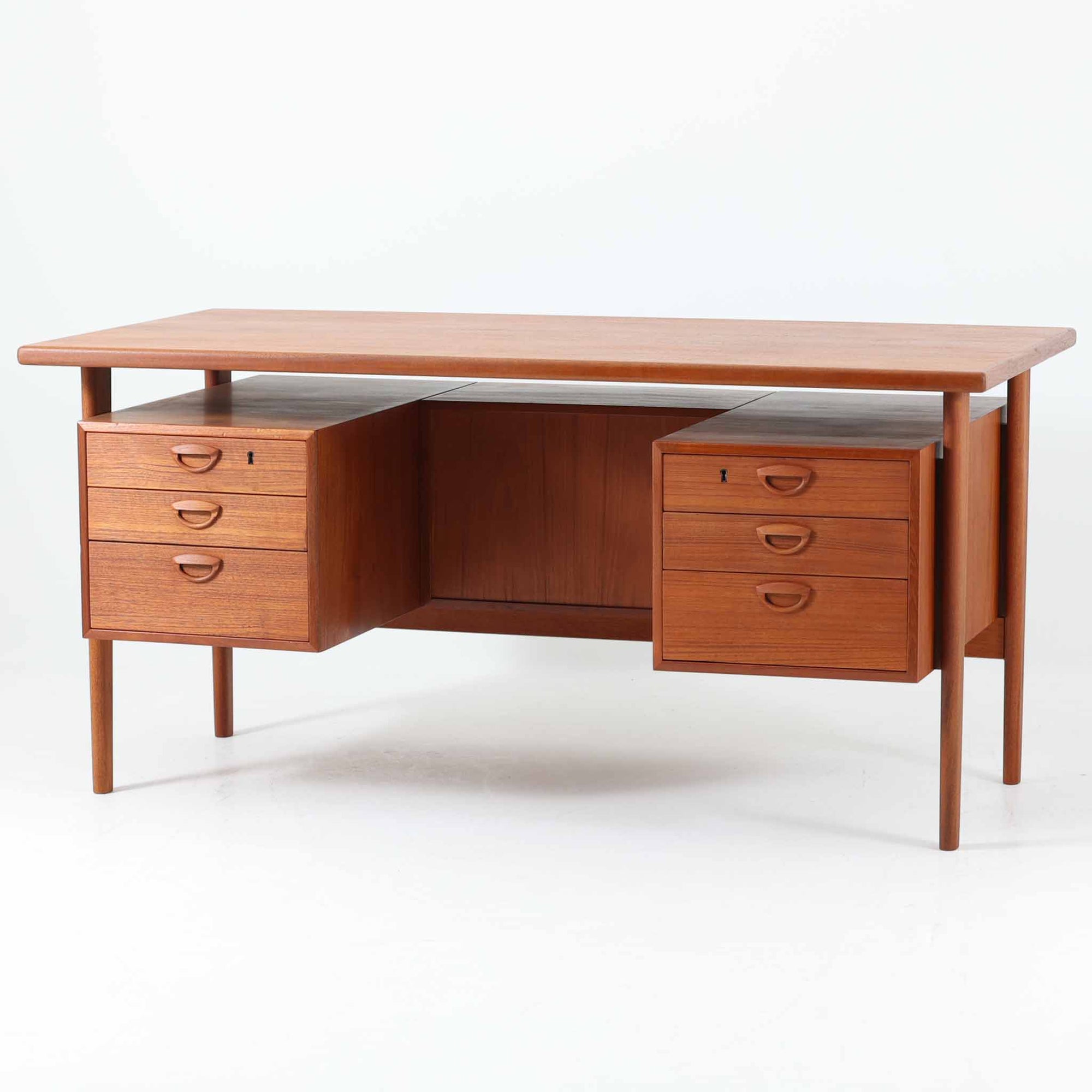 カイ・クリスチャンセンがデザインし、FM furniture社によって製造されたこちらの両袖デスクは、チーク材の美しい木目と温かみのある色合いが魅力の北欧ビンテージ家具です。左右には3杯ずつの引き出し、中央には扉付き収納を備え、背面にはオープンシェルフが設けられており、デスクとしての高い収納力と機能性を誇ります。壁付けはもちろん、間仕切りとしても活用できるため、空間の中心にも映える設計です。丸みを帯びた取手や脚部など、細部にまでこだわった意匠は、カイ・クリスチャンセンらしい洗練された美しさを体現しており、上質なワークスペースを演出します。