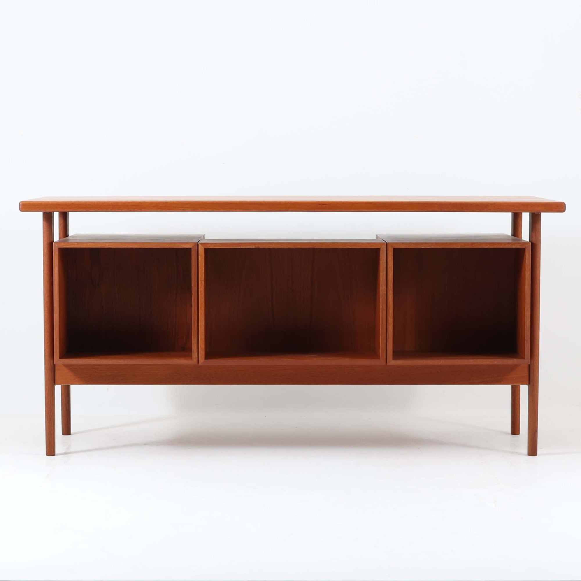 カイ・クリスチャンセンがデザインし、FM furniture社によって製造されたこちらの両袖デスクは、チーク材の美しい木目と温かみのある色合いが魅力の北欧ビンテージ家具です。左右には3杯ずつの引き出し、中央には扉付き収納を備え、背面にはオープンシェルフが設けられており、デスクとしての高い収納力と機能性を誇ります。壁付けはもちろん、間仕切りとしても活用できるため、空間の中心にも映える設計です。丸みを帯びた取手や脚部など、細部にまでこだわった意匠は、カイ・クリスチャンセンらしい洗練された美しさを体現しており、上質なワークスペースを演出します。