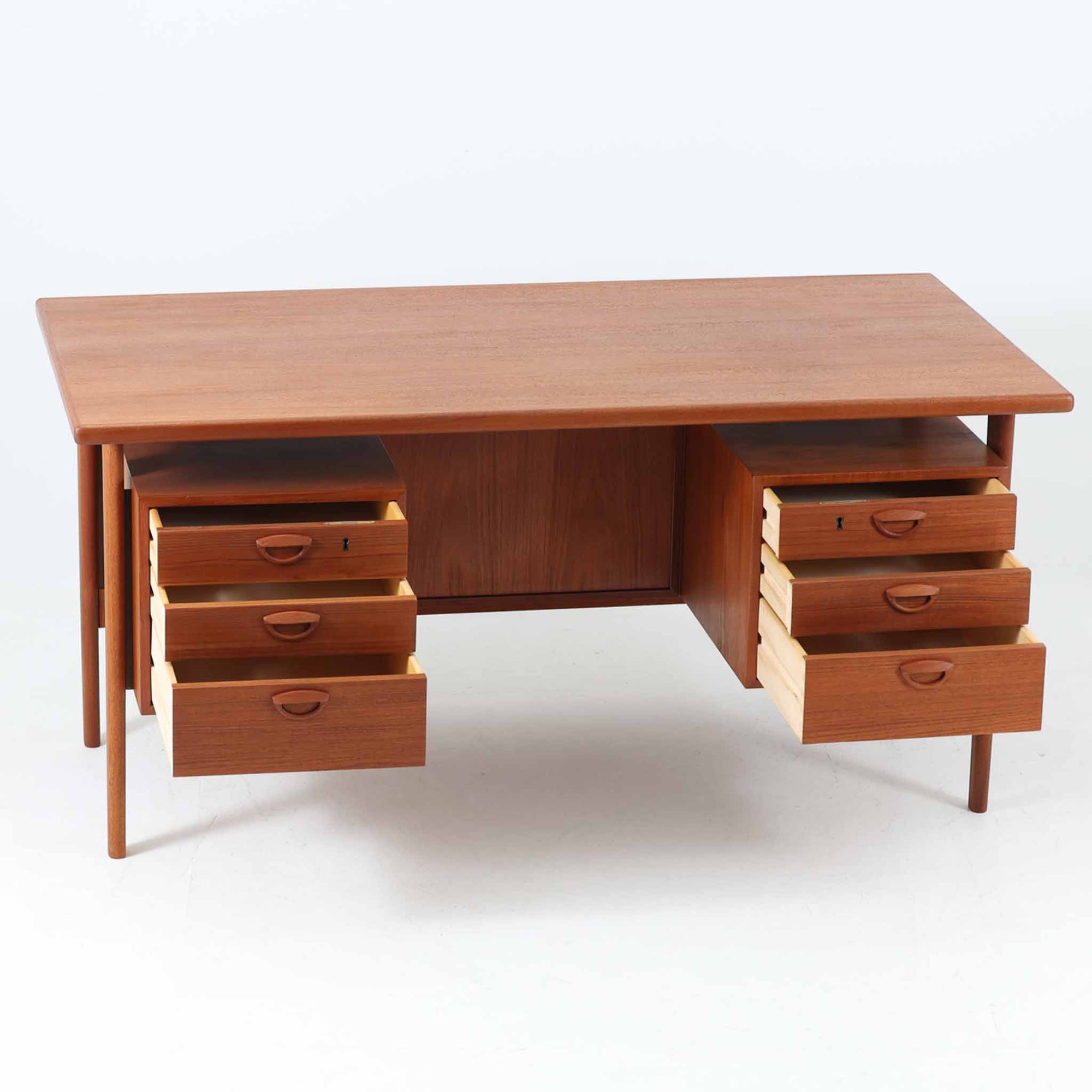 カイ・クリスチャンセンがデザインし、FM furniture社によって製造されたこちらの両袖デスクは、チーク材の美しい木目と温かみのある色合いが魅力の北欧ビンテージ家具です。左右には3杯ずつの引き出し、中央には扉付き収納を備え、背面にはオープンシェルフが設けられており、デスクとしての高い収納力と機能性を誇ります。壁付けはもちろん、間仕切りとしても活用できるため、空間の中心にも映える設計です。丸みを帯びた取手や脚部など、細部にまでこだわった意匠は、カイ・クリスチャンセンらしい洗練された美しさを体現しており、上質なワークスペースを演出します。