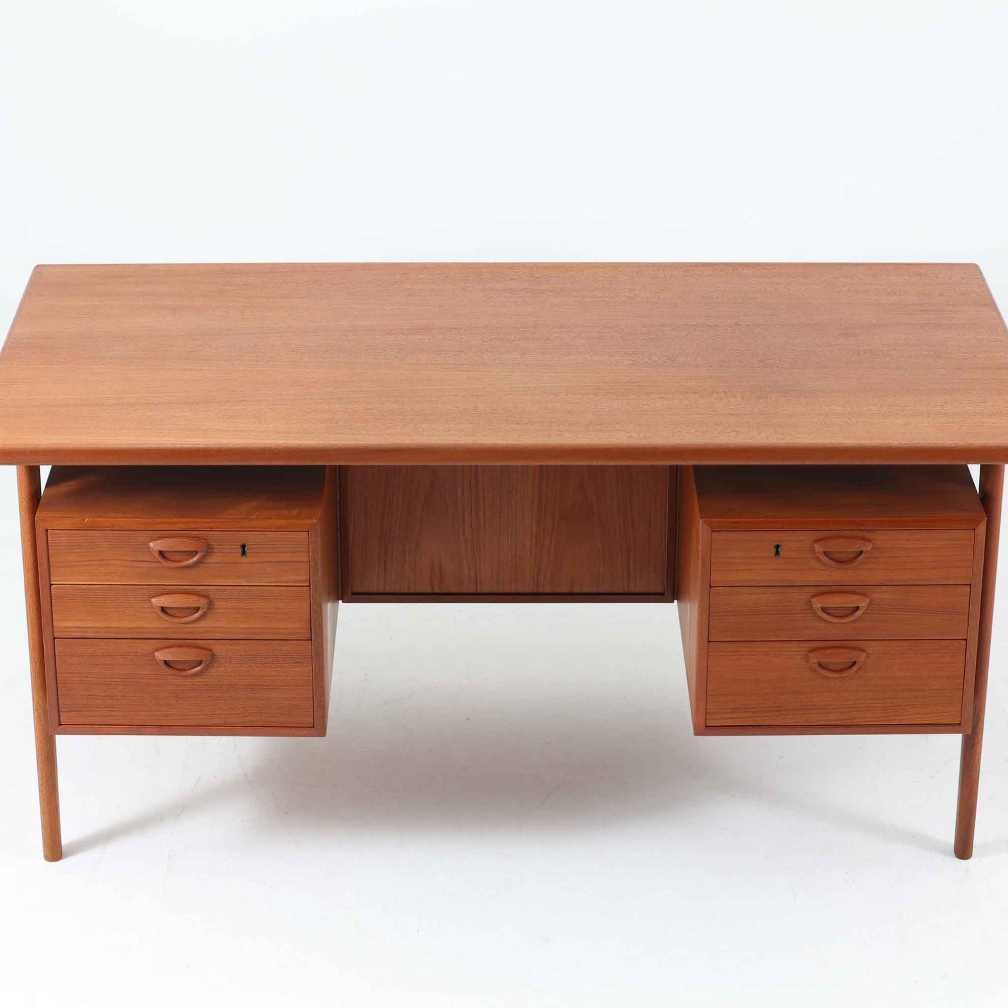 カイ・クリスチャンセンがデザインし、FM furniture社によって製造されたこちらの両袖デスクは、チーク材の美しい木目と温かみのある色合いが魅力の北欧ビンテージ家具です。左右には3杯ずつの引き出し、中央には扉付き収納を備え、背面にはオープンシェルフが設けられており、デスクとしての高い収納力と機能性を誇ります。壁付けはもちろん、間仕切りとしても活用できるため、空間の中心にも映える設計です。丸みを帯びた取手や脚部など、細部にまでこだわった意匠は、カイ・クリスチャンセンらしい洗練された美しさを体現しており、上質なワークスペースを演出します。