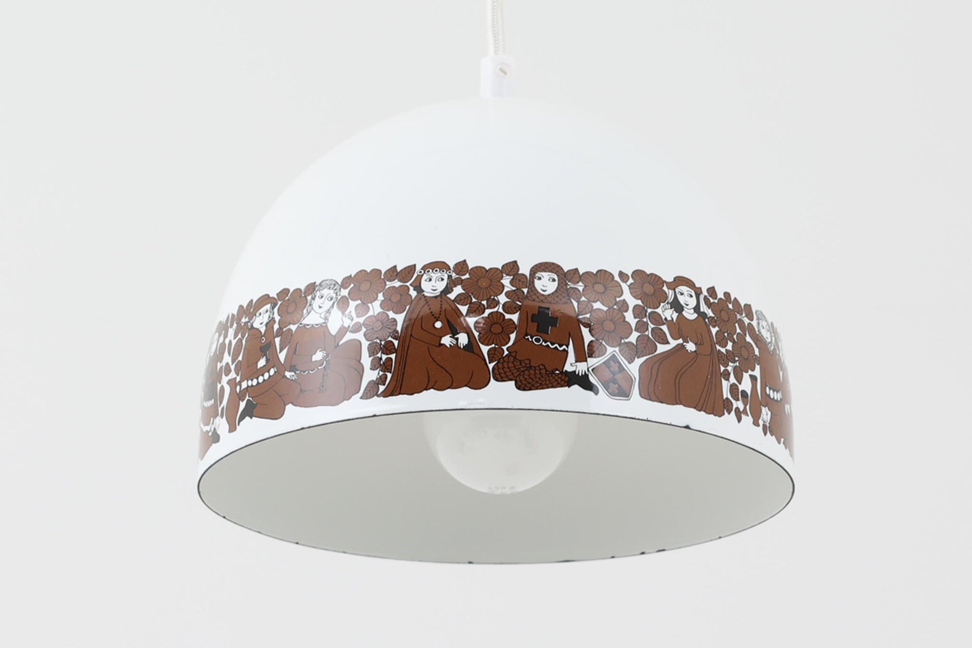 フィンランドの名窯ARABIA（アラビア）社によるRITARI（リタリ）シリーズのビンテージランプシェードです。柔らかなカーブを描くドーム型のフォルムは、フィンランドモダンを代表するデザイナーKaj Franck（カイ・フランク）によるもので、花と人物が描かれた印象的な装飾はRaija Uosikkinen（ライヤ・ウオシッキネン）によってデザインされました。RITARIはフィンランド語で「騎士」を意味し、中世の衣装をまとった人物たちが、ブラウンを基調とした花々とともにシェードをぐるりと囲むユニークでノスタルジックなデザインが特徴です。素材はホーロー（琺瑯）製で、しっかりとした重量感と経年による独特の風合いも楽しめるアイテム。点灯時にはやわらかな光を下方向に届け、空間に温もりを添えてくれます。北欧らしいストーリー性とデザイン性を併せ持った、希少なビンテージ照明をお探しの方におすすめです。