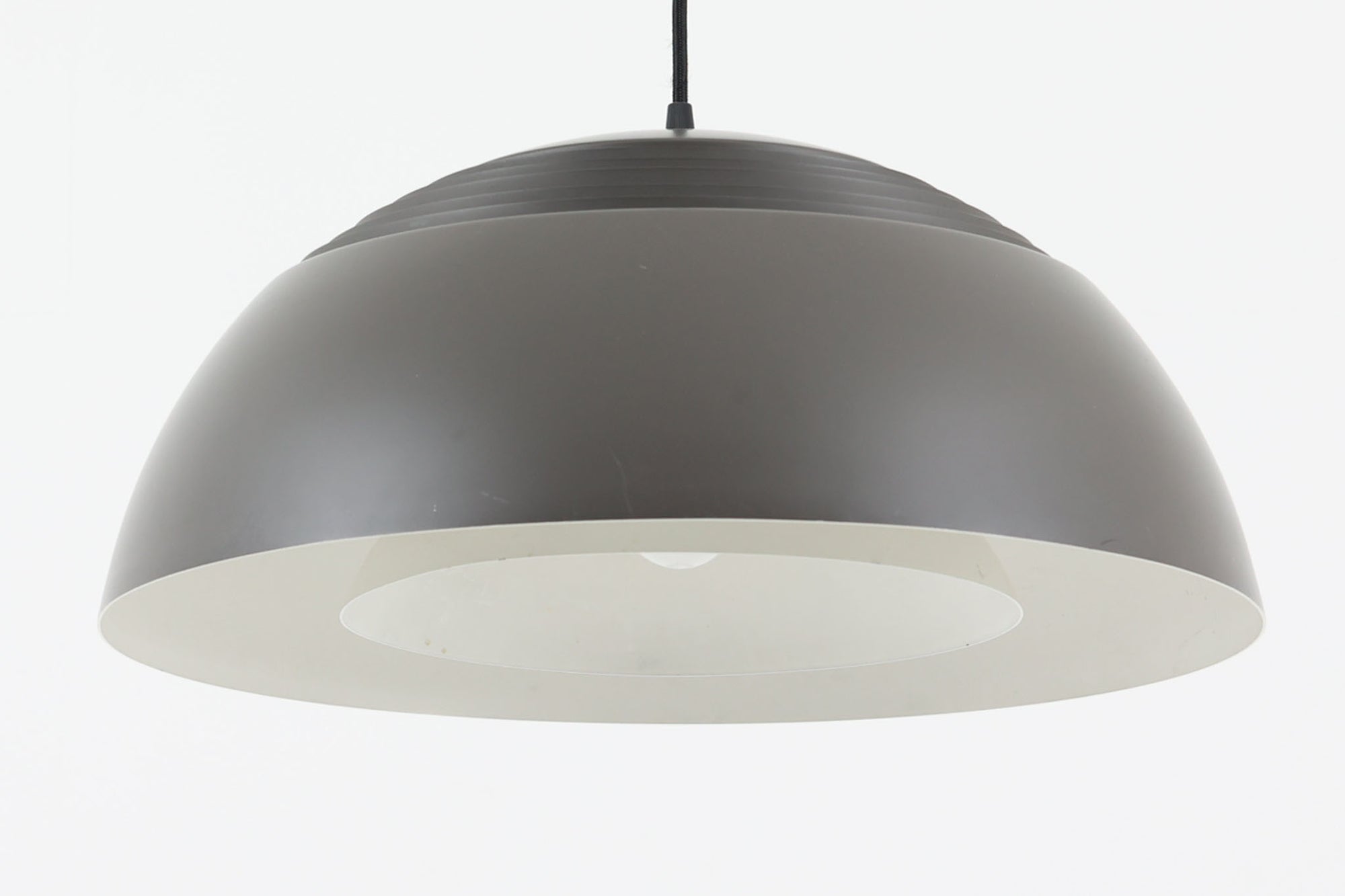アルネ・ヤコブセンによってデザインされ、Louis Poulsen（ルイスポールセン）より製造されたAJロイヤル ペンダントライト。こちらは希少なグラファイトグレーカラーで、落ち着いたトーンが空間にシックな雰囲気を演出します。直径50cmの大型サイズで、光源を遮る構造と放射状に配置されたルーバーにより、眩しさを抑えた柔らかい光が空間全体を包み込みます。点灯時には上部のスリットから漏れる光も美しく、デザイン性と機能性を兼ね備えた一品です。外観には小傷や使用感がありますが、ビンテージならではの風合いとしてお楽しみいただけます。