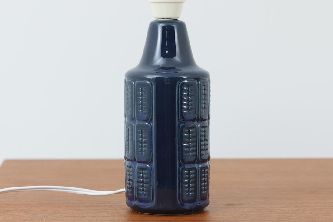 デンマークの陶器ブランドDesiree（デシレ）によって制作されたヴィンテージのテーブルランプ。深みのあるネイビーブルーの艶やかな釉薬に、規則正しく並んだ凹凸のある幾何学模様が印象的なデザインです。スリムな円筒形のフォルムは空間にすっきりと馴染みつつ、どこかグラフィカルな存在感を漂わせます。底部には「Desiree Stentoj – Denmark」の刻印と品番が施されています。シェードには新品のリネン製シェードを使用し、光をやわらかく透過。北欧ヴィンテージらしいモダンさと温もりを兼ね備えた一灯です。