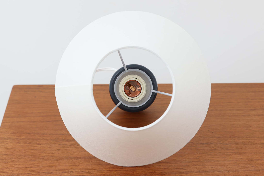デンマークの陶器ブランドDesiree（デシレ）によって制作されたヴィンテージのテーブルランプ。深みのあるネイビーブルーの艶やかな釉薬に、規則正しく並んだ凹凸のある幾何学模様が印象的なデザインです。スリムな円筒形のフォルムは空間にすっきりと馴染みつつ、どこかグラフィカルな存在感を漂わせます。底部には「Desiree Stentoj – Denmark」の刻印と品番が施されています。シェードには新品のリネン製シェードを使用し、光をやわらかく透過。北欧ヴィンテージらしいモダンさと温もりを兼ね備えた一灯です。
