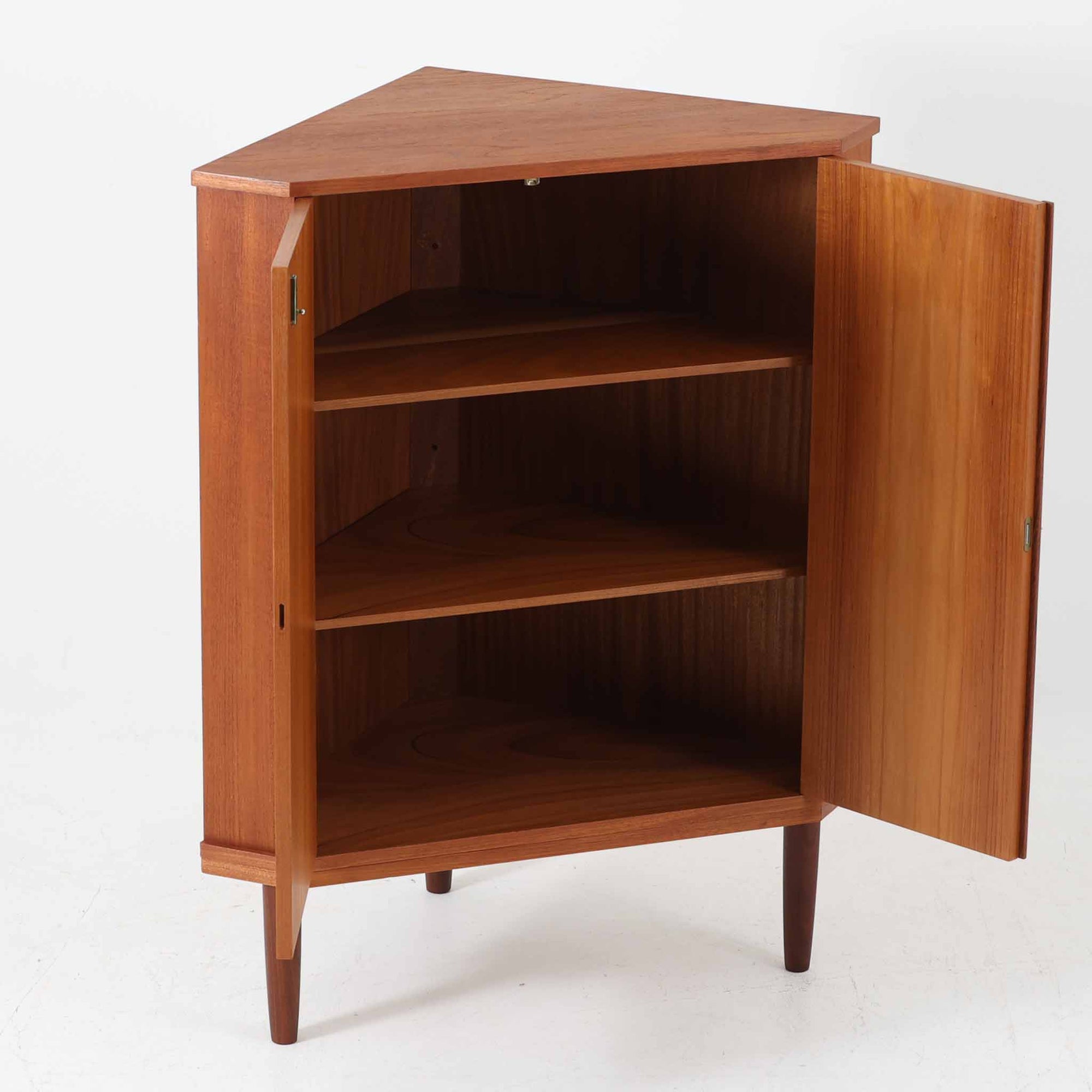 三角形のユニークなフォルムが目を引くこちらのコーナーキャビネットは、デンマーク製の北欧ビンテージ家具です。チーク材の温もりある木肌と、鍵付きのシンメトリーな扉が上品な佇まいを演出します。内部には棚板が2枚設けられており、日用品や雑貨などの収納に実用的。空間の角にすっきりと収まる設計は、デッドスペースを活かしながら、インテリアに程よいアクセントを加えてくれます。シンプルながら希少性を感じさせる一台です。