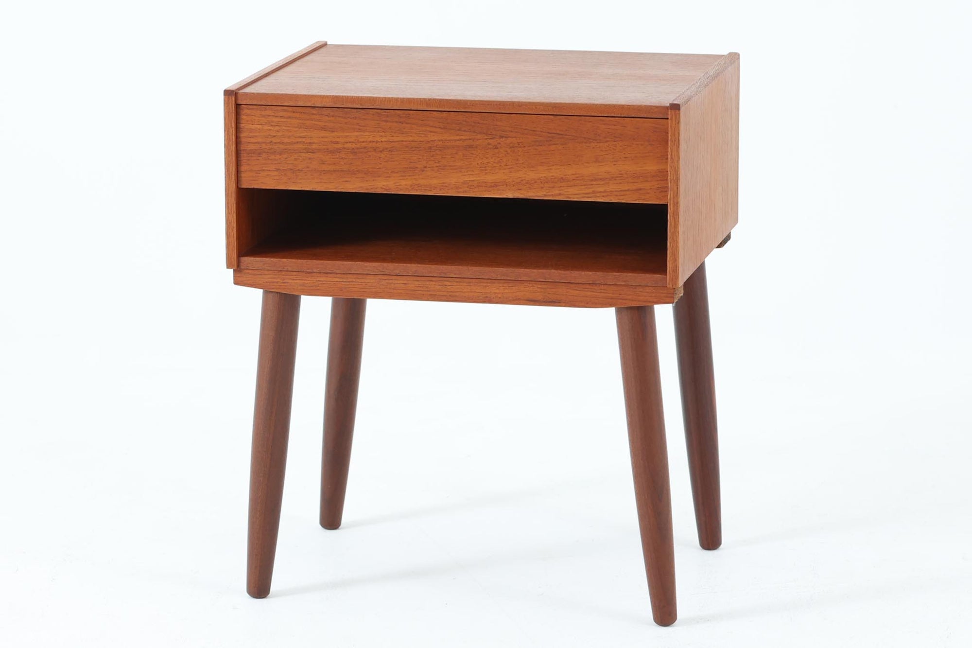 デンマークで製造されたヴィンテージのサイドチェスト。温もりのあるチーク材を用いた本体に、先細りの丸脚を組み合わせた軽やかな佇まいが魅力です。引き出し1杯に加え、下部にはオープンスペースを備えており、リモコンや文庫本などをすぐに取り出せる実用的な構造。天板や側面にはすっきりとした面取りが施され、シンプルなデザインの中に丁寧な仕事が感じられます。北欧らしいあたたかみと実用性を兼ね備えた一台。ベッドサイドはもちろん、リビングや玄関先など、暮らしのさまざまな場面で活躍します。