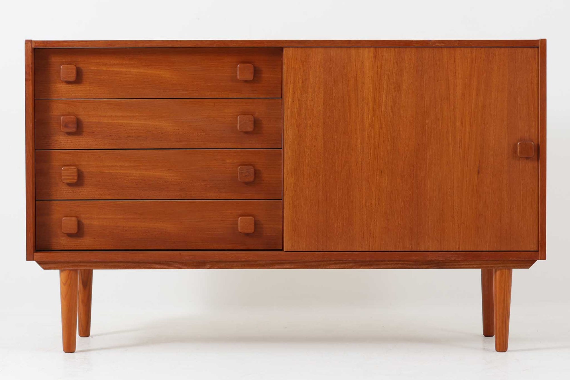 Domino Mobler社によって製造されたチーク材のサイドボードは、北欧ビンテージ家具らしいシンプルながらも洗練された佇まいが魅力です。美しい木目と質感のあるチーク材が上品な存在感を放ち、引き出しと扉収納の組み合わせにより実用性にも優れています。丸みを帯びた取手のデザインも丁寧に設計されており、ヴィンテージならではの趣を感じさせる一台です。リビングの収納やテレビボードとして、幅広いシーンで活躍します。