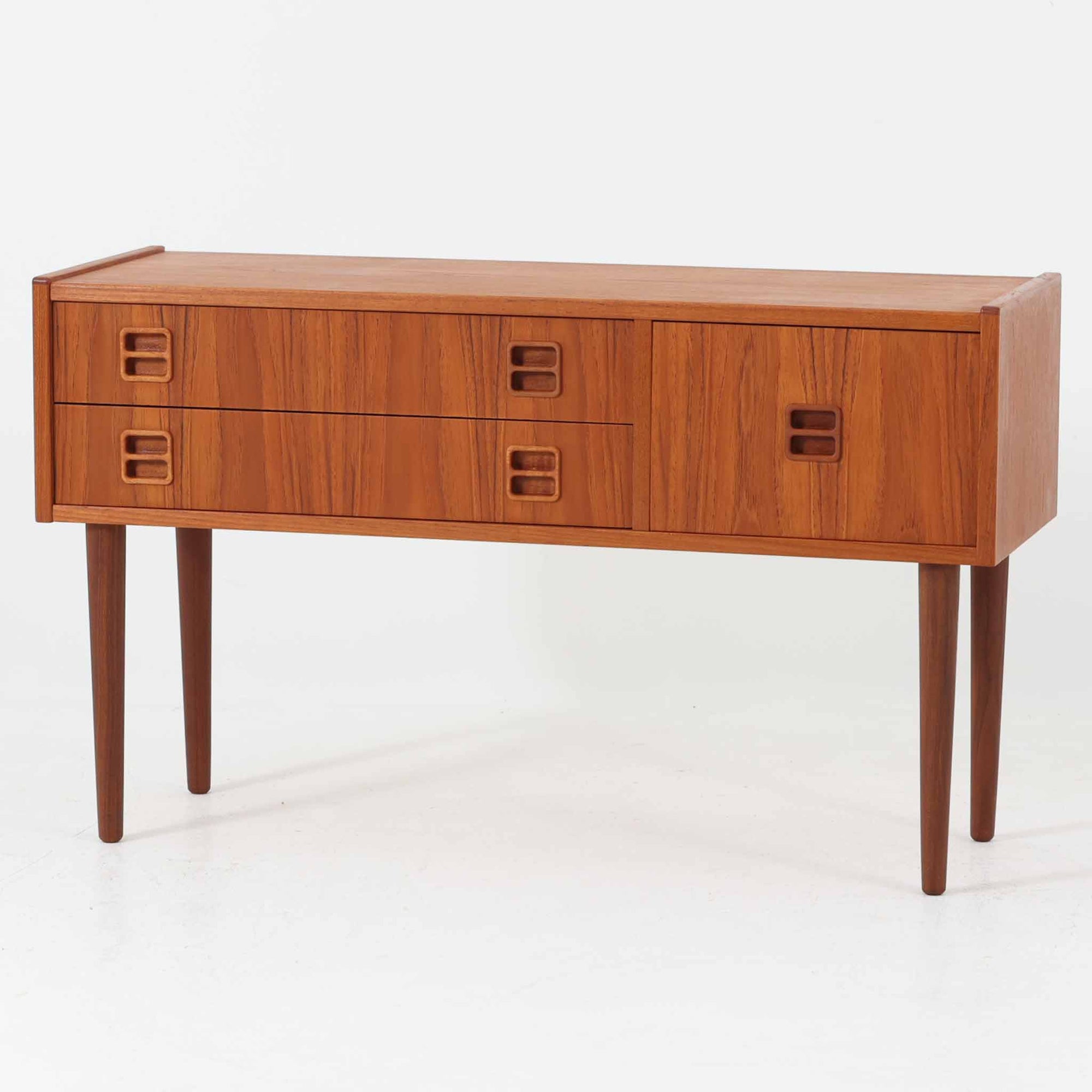 前板に施された彫り込み取手が印象的なこちらの多段チェストは、チーク材の美しい木目と引き締まったフォルムが特徴的で、幅89cmという程よいサイズ感に加え、3杯の引き出しが異なる深さで構成されており、収納力と実用性の高い北欧ビンテージ家具です。細身の脚部が全体を軽やかに見せ、玄関先やリビングのサイド収納としても活躍します。