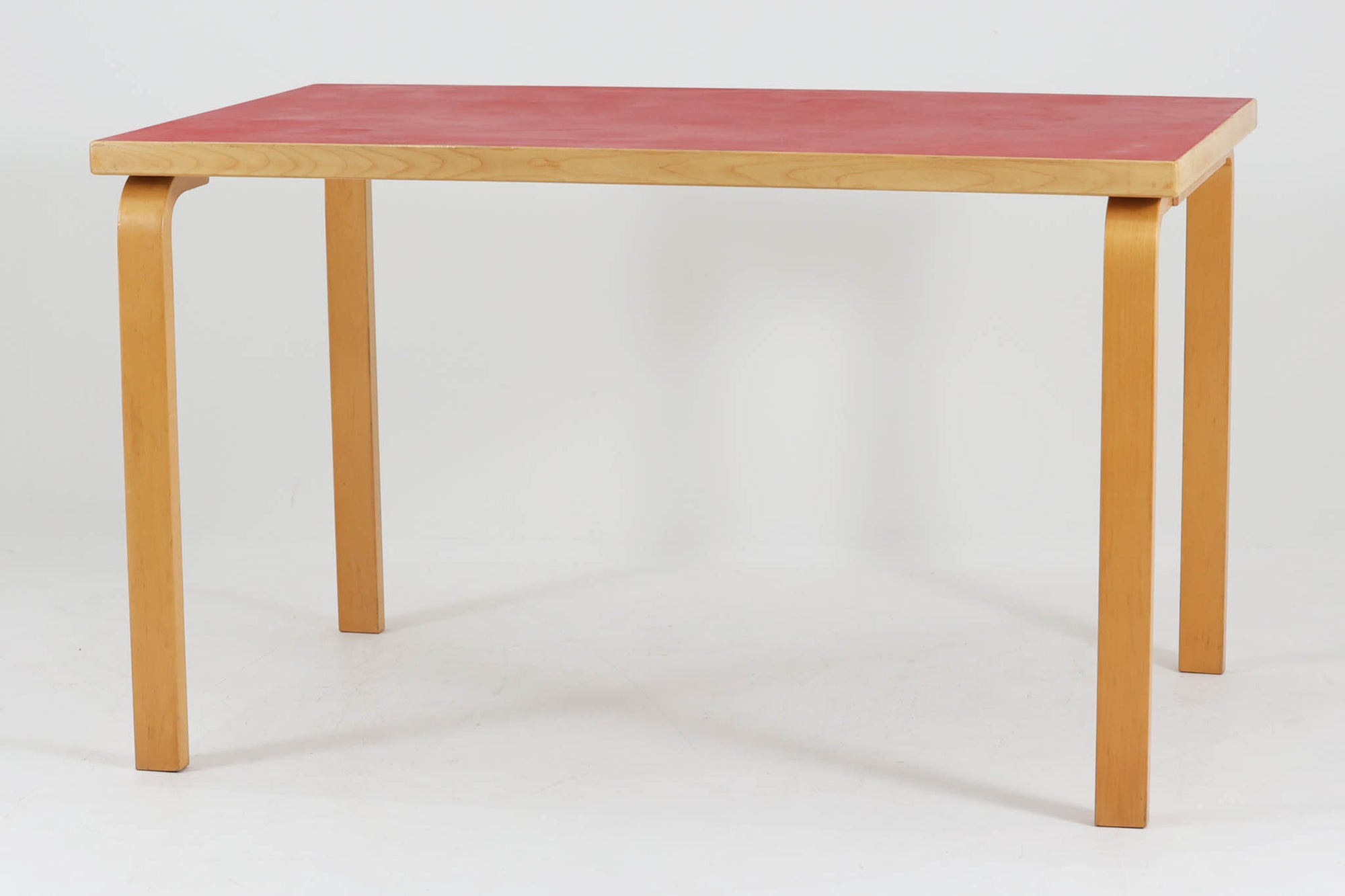 Artek社による、Alvar Aaltoデザインの幅120cmのダイニングテーブル。1970～1980年代に製造されたと考えられるヴィンテージ品です。Aaltoらしい流れるような曲線と、機能美を兼ね備えたデザインが特徴的。天板にはリノリウムが施されており、落ち着いたマットな質感と耐久性を備えています。温かみのあるバーチ材のフレームと、鮮やかなレッドの天板が美しいコントラストを生み出し、空間に独特の存在感を与えます。シンプルでありながら洗練された佇まいは、北欧デザインの魅力を存分に感じさせる一台です。