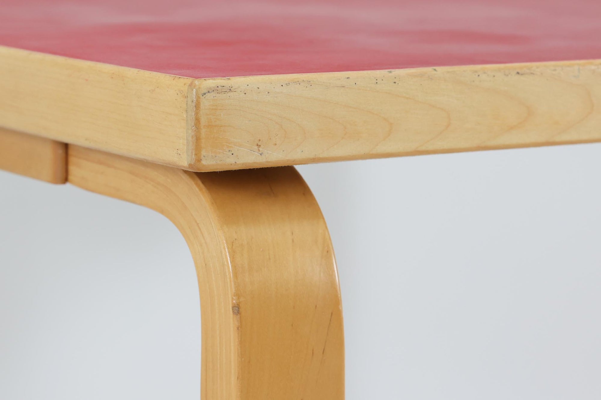 Artek社による、Alvar Aaltoデザインの幅120cmのダイニングテーブル。1970～1980年代に製造されたと考えられるヴィンテージ品です。Aaltoらしい流れるような曲線と、機能美を兼ね備えたデザインが特徴的。天板にはリノリウムが施されており、落ち着いたマットな質感と耐久性を備えています。温かみのあるバーチ材のフレームと、鮮やかなレッドの天板が美しいコントラストを生み出し、空間に独特の存在感を与えます。シンプルでありながら洗練された佇まいは、北欧デザインの魅力を存分に感じさせる一台です。