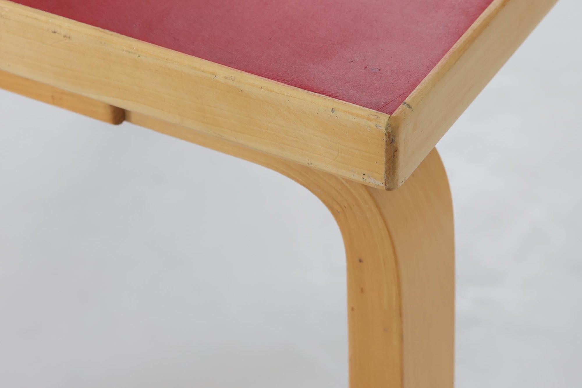 Artek社による、Alvar Aaltoデザインの幅120cmのダイニングテーブル。1970～1980年代に製造されたと考えられるヴィンテージ品です。Aaltoらしい流れるような曲線と、機能美を兼ね備えたデザインが特徴的。天板にはリノリウムが施されており、落ち着いたマットな質感と耐久性を備えています。温かみのあるバーチ材のフレームと、鮮やかなレッドの天板が美しいコントラストを生み出し、空間に独特の存在感を与えます。シンプルでありながら洗練された佇まいは、北欧デザインの魅力を存分に感じさせる一台です。