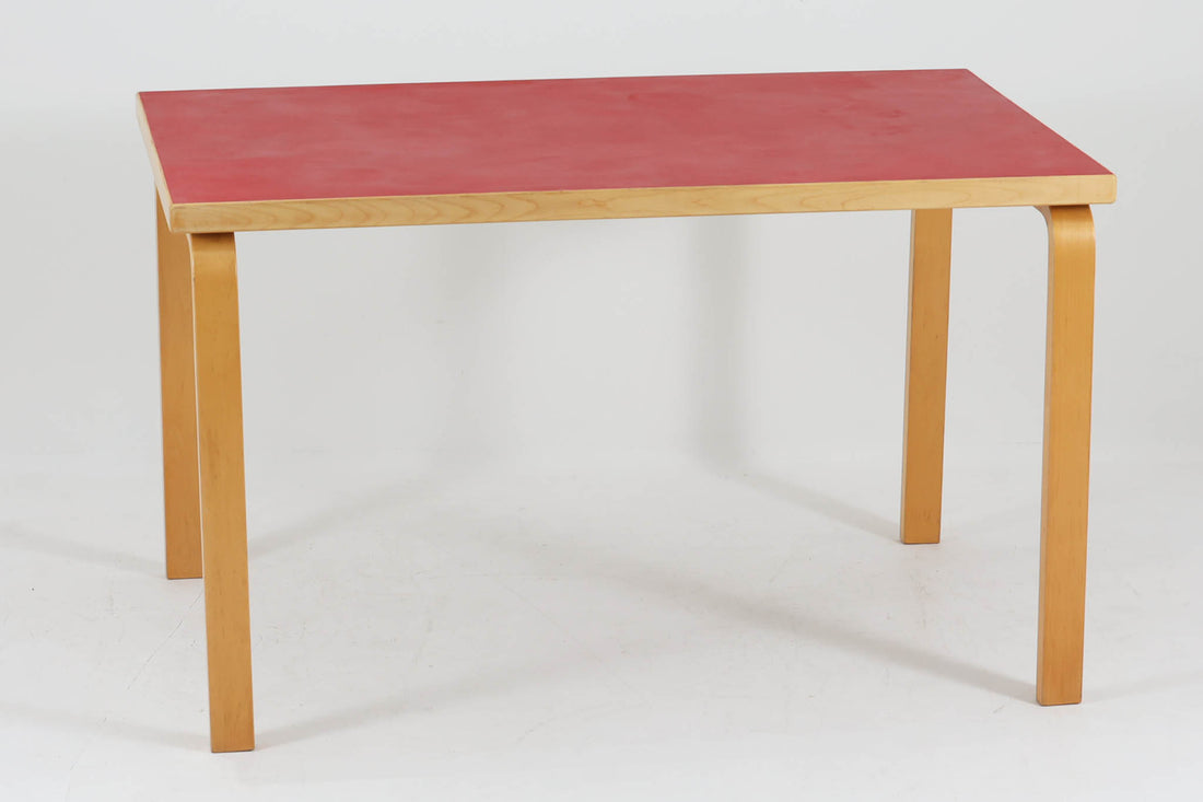 Artek社による、Alvar Aaltoデザインの幅120cmのダイニングテーブル。1970～1980年代に製造されたと考えられるヴィンテージ品です。Aaltoらしい流れるような曲線と、機能美を兼ね備えたデザインが特徴的。天板にはリノリウムが施されており、落ち着いたマットな質感と耐久性を備えています。温かみのあるバーチ材のフレームと、鮮やかなレッドの天板が美しいコントラストを生み出し、空間に独特の存在感を与えます。シンプルでありながら洗練された佇まいは、北欧デザインの魅力を存分に感じさせる一台です。
