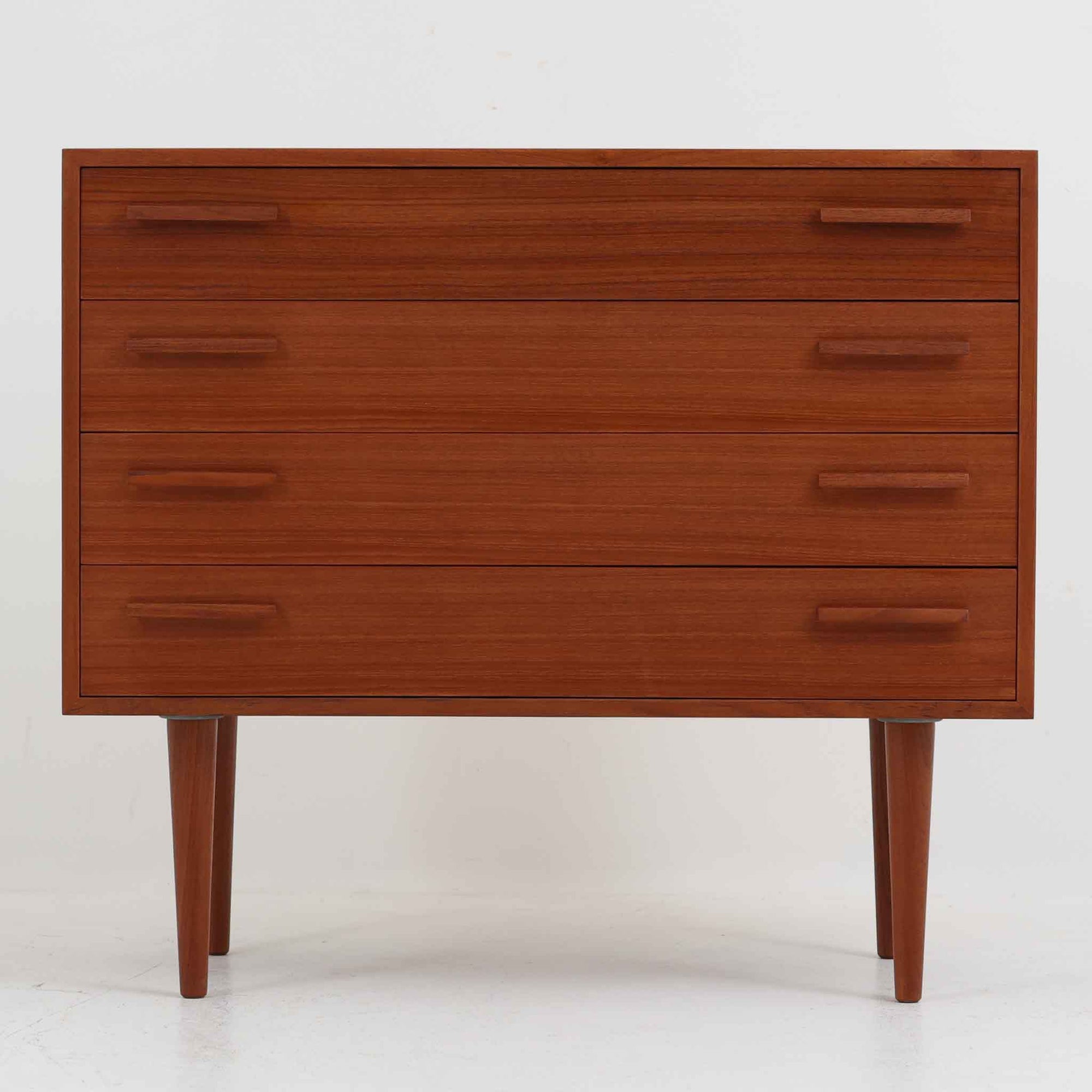 Kai Kristiansen（カイ・クリスチャンセン）によるデザインで、Feldballes Mobelfabrik社から製造された4段チェストです。端正なチーク材の木目と、すっきりとした直線構成が美しく調和し、北欧デザインらしい静かな上質さを感じさせます。細身のテーパー脚が軽やかな印象を与えつつ、引き出しの厚みや無垢材の取っ手が確かな存在感を放ちます。幅86cmの程よいサイズで、寝室やリビングの収納家具としても最適。経年によって深みを増したチーク材の艶が、ビンテージならではの味わいを引き立てています。