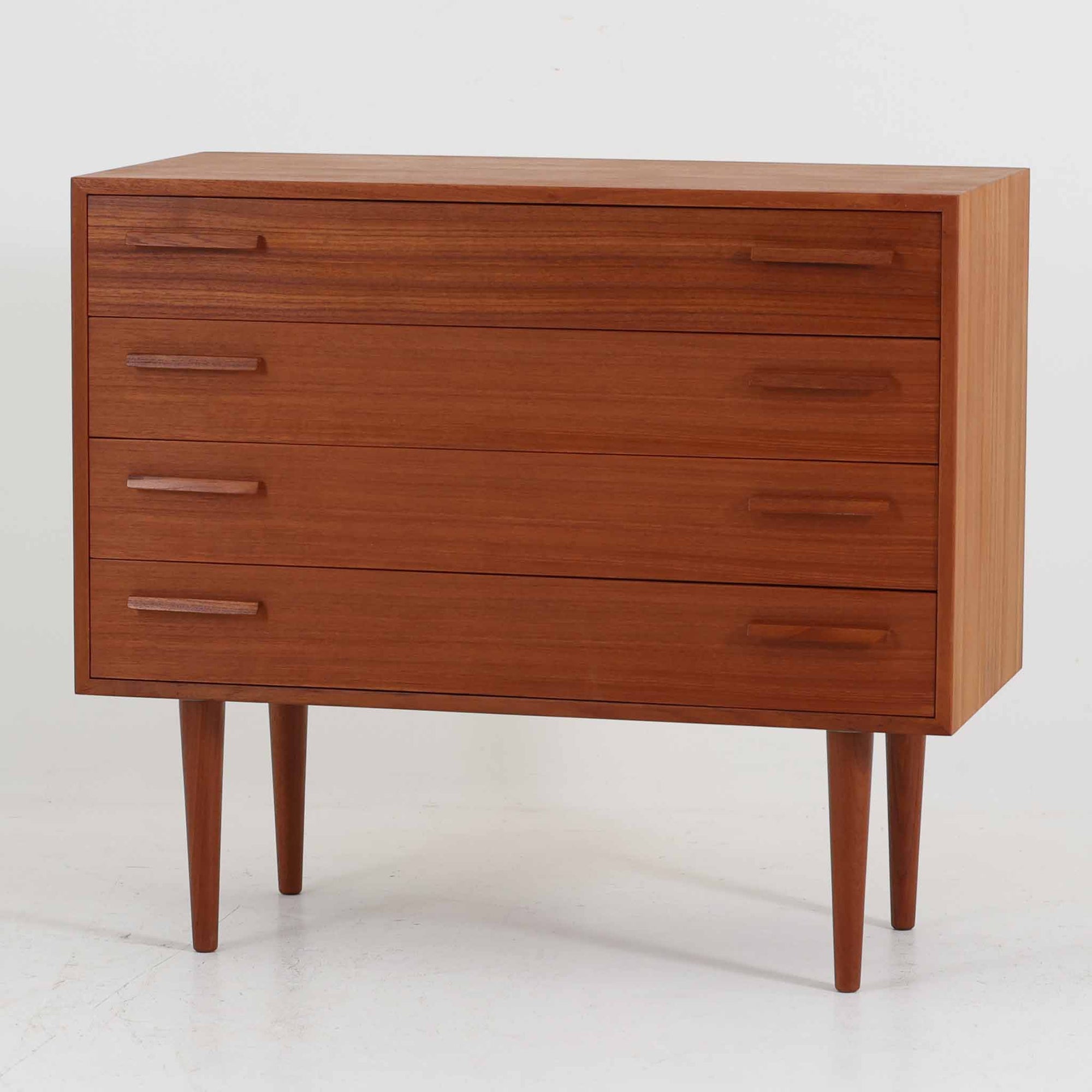 Kai Kristiansen（カイ・クリスチャンセン）によるデザインで、Feldballes Mobelfabrik社から製造された4段チェストです。端正なチーク材の木目と、すっきりとした直線構成が美しく調和し、北欧デザインらしい静かな上質さを感じさせます。細身のテーパー脚が軽やかな印象を与えつつ、引き出しの厚みや無垢材の取っ手が確かな存在感を放ちます。幅86cmの程よいサイズで、寝室やリビングの収納家具としても最適。経年によって深みを増したチーク材の艶が、ビンテージならではの味わいを引き立てています。