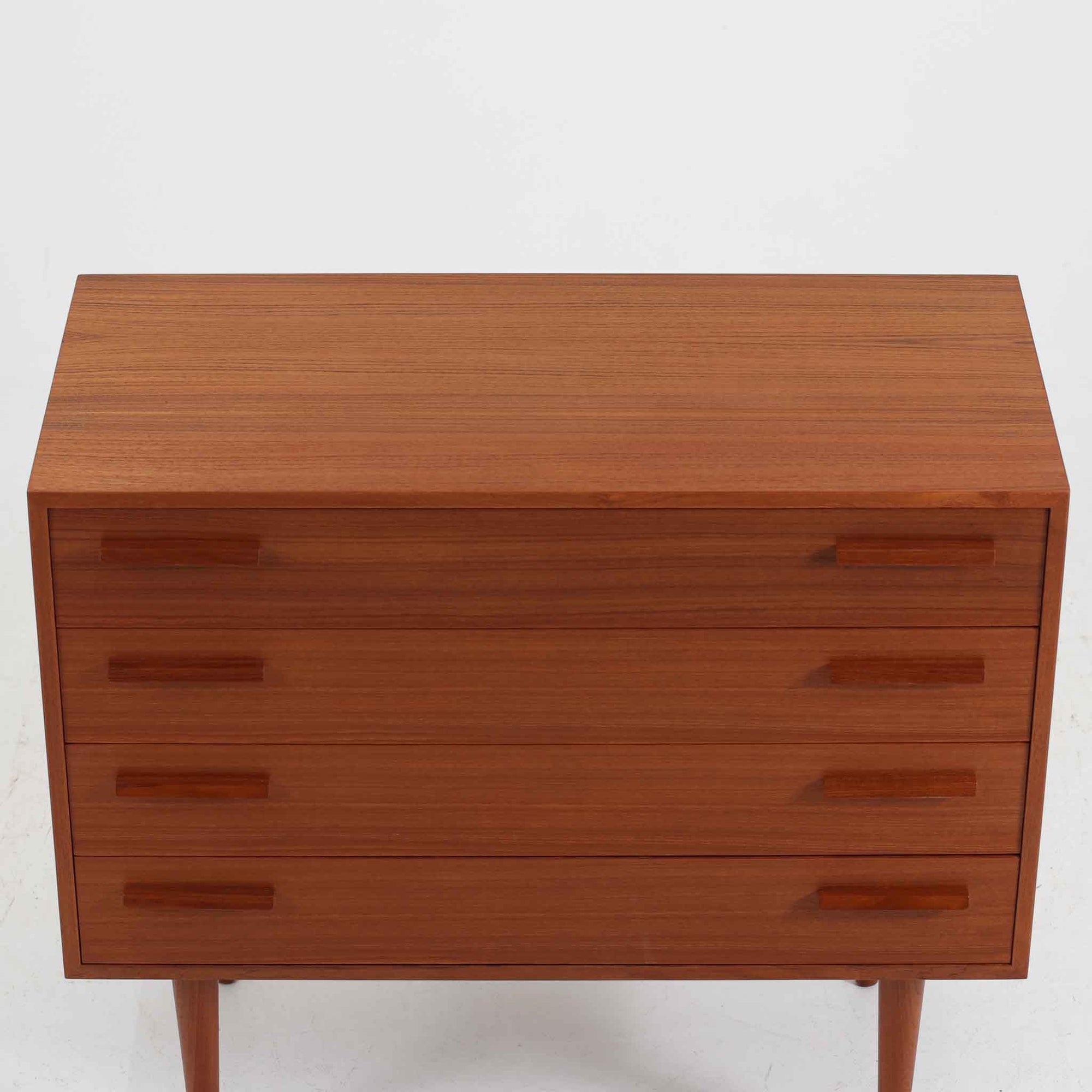 Kai Kristiansen（カイ・クリスチャンセン）によるデザインで、Feldballes Mobelfabrik社から製造された4段チェストです。端正なチーク材の木目と、すっきりとした直線構成が美しく調和し、北欧デザインらしい静かな上質さを感じさせます。細身のテーパー脚が軽やかな印象を与えつつ、引き出しの厚みや無垢材の取っ手が確かな存在感を放ちます。幅86cmの程よいサイズで、寝室やリビングの収納家具としても最適。経年によって深みを増したチーク材の艶が、ビンテージならではの味わいを引き立てています。
