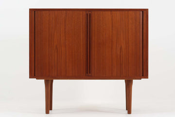 デンマークのデザイナー、Kai Kristiansen（カイ・クリスチャンセン）によってデザインされた、Fm furniture社製のビンテージキャビネットです。素材には上質なチーク材が用いられており、深みのある美しい木目とあたたかみのある色合いが魅力です。フロントには、機能性とデザイン性を兼ね備えた蛇腹扉が採用されており、開閉の動作そのものが楽しめる一台です。内部にはフェルトが敷かれた引き出し2段と収納スペースがあり、カトラリーや書類、小物の整理にも最適です。高さのある丸脚は、北欧家具らしい軽やかな印象を与えながらも、根元にかけてややふくらみを持たせた独特のフォルムとなっており、全体のデザイン性を高めています。コンパクトなサイズ感は空間を圧迫せず、リビングや玄関、書斎など様々なシーンに馴染みます。北欧デザインの美しさと実用性を兼ね備えたキャビネットです。