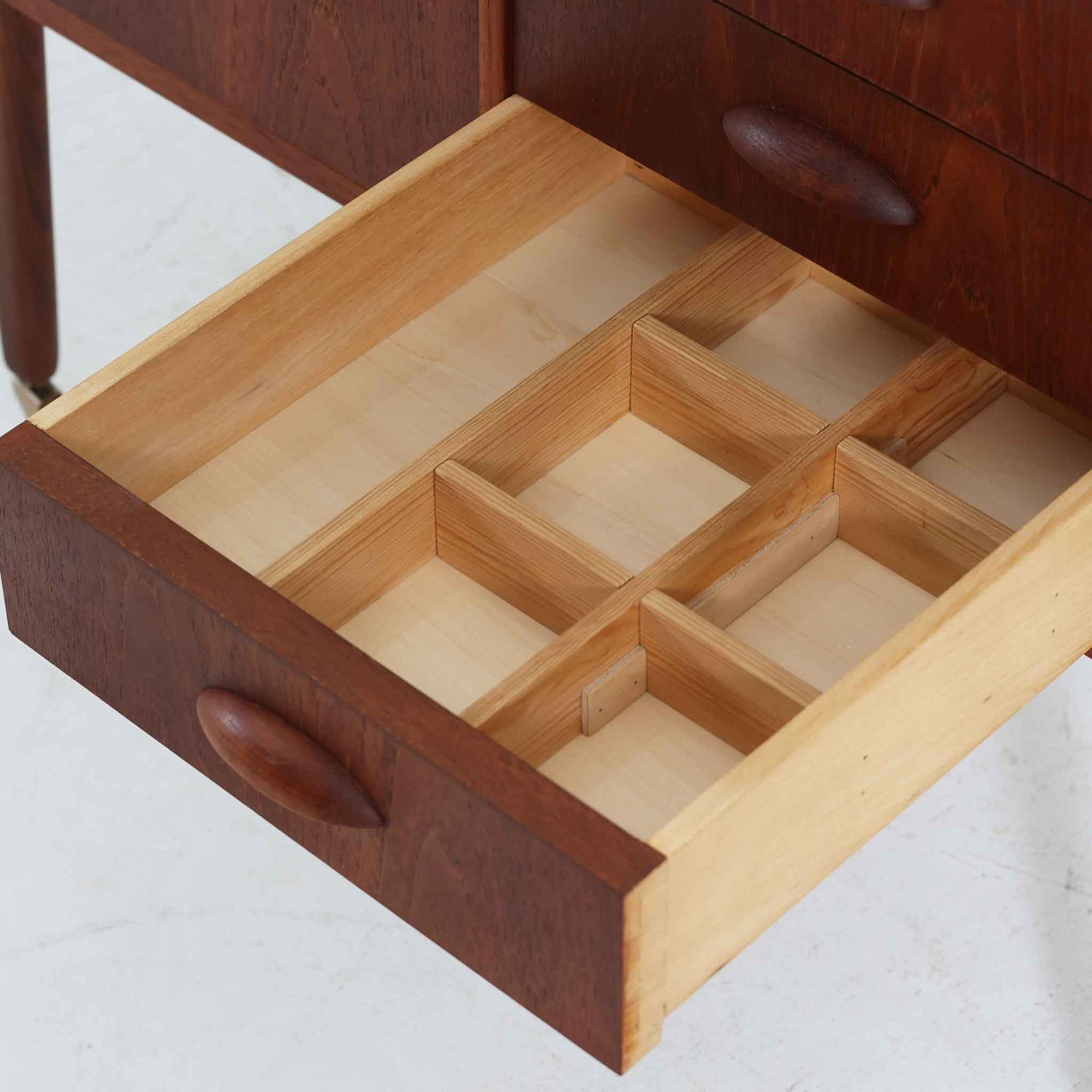 チーク材を使用したデンマーク製のソーイングテーブルです。丸みを帯びた脚部と有機的な取っ手のデザインが愛らしく、温かみのある木目が上品な印象を与えます。引き出し内には仕切りが設けられ、小物の整理にも便利。キャスター付きで移動もスムーズに行えます。ミシン台や裁縫用としてはもちろん、リビングでサイドテーブルや収納台としても活躍する汎用性の高い一台です。経年によるチークの深い色艶が、北欧ビンテージ家具ならではの趣を添えています。