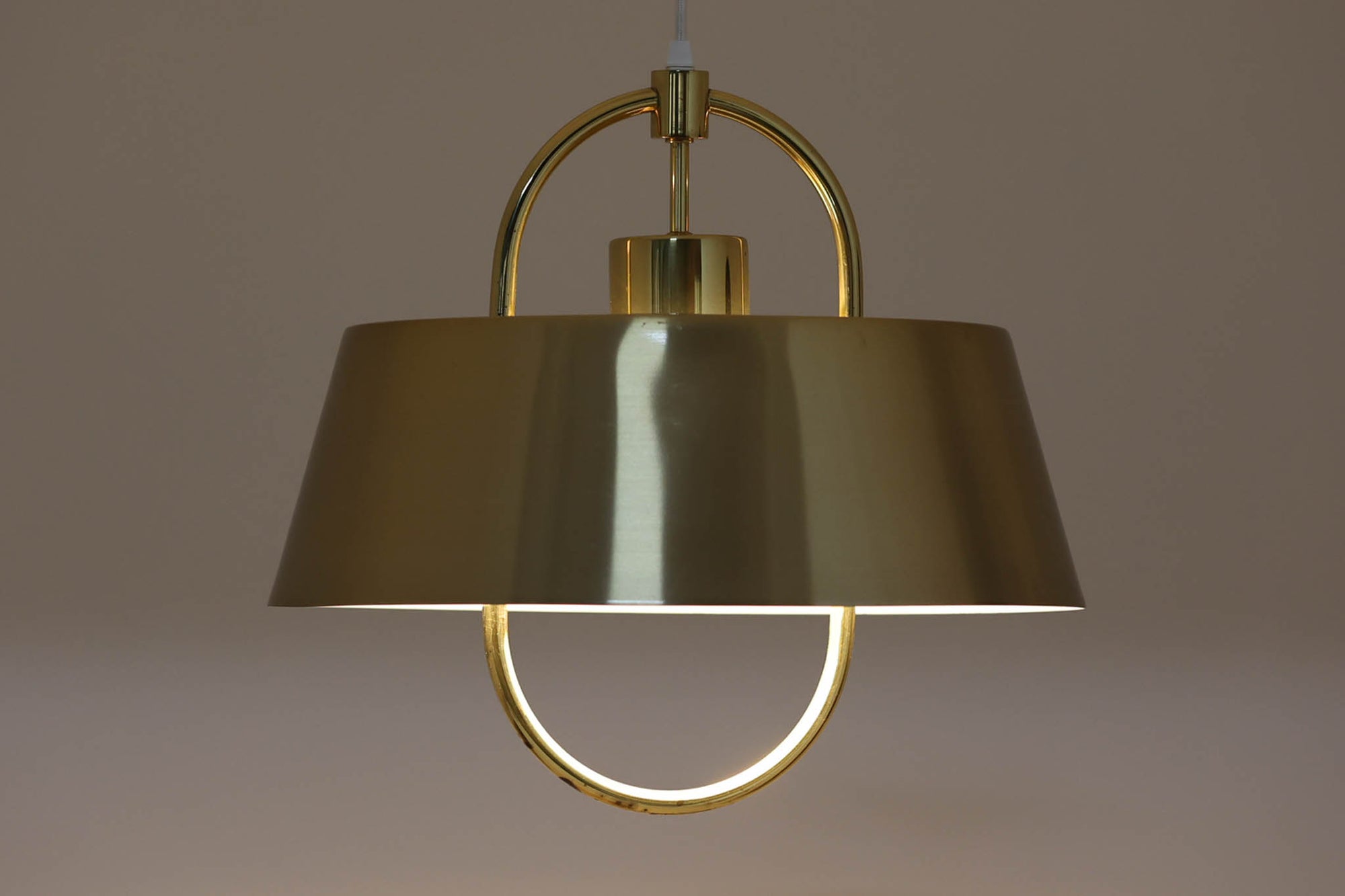 デンマークの照明ブランド、Fog & morup（フォグ＆モーラップ）社によるペンダントライト「Hercules」。デザインは同社を代表するデザイナー、Jo Hammerborg（ヨー・ハーマボー）。直径41cmの存在感あるサイズに、上下を弧状に囲む真鍮製のアームが印象的な構造で、点灯時には下部のリングが光を受けて柔らかく浮かび上がります。外側はゴールドブラス、内側はホワイトで塗装されており、光の反射を美しく拡散させる仕様です。経年により一部にくすみや細かなキズが見られますが、全体としては美しい輝きを保っており、ビンテージならではの雰囲気を楽しめる一点です。E26口金のLED電球に対応し、現代の生活空間でも安心してご使用いただけます。北欧ミッドセンチュリーデザインの象徴的な一灯として、リビングやダイニングのアクセントにおすすめです。