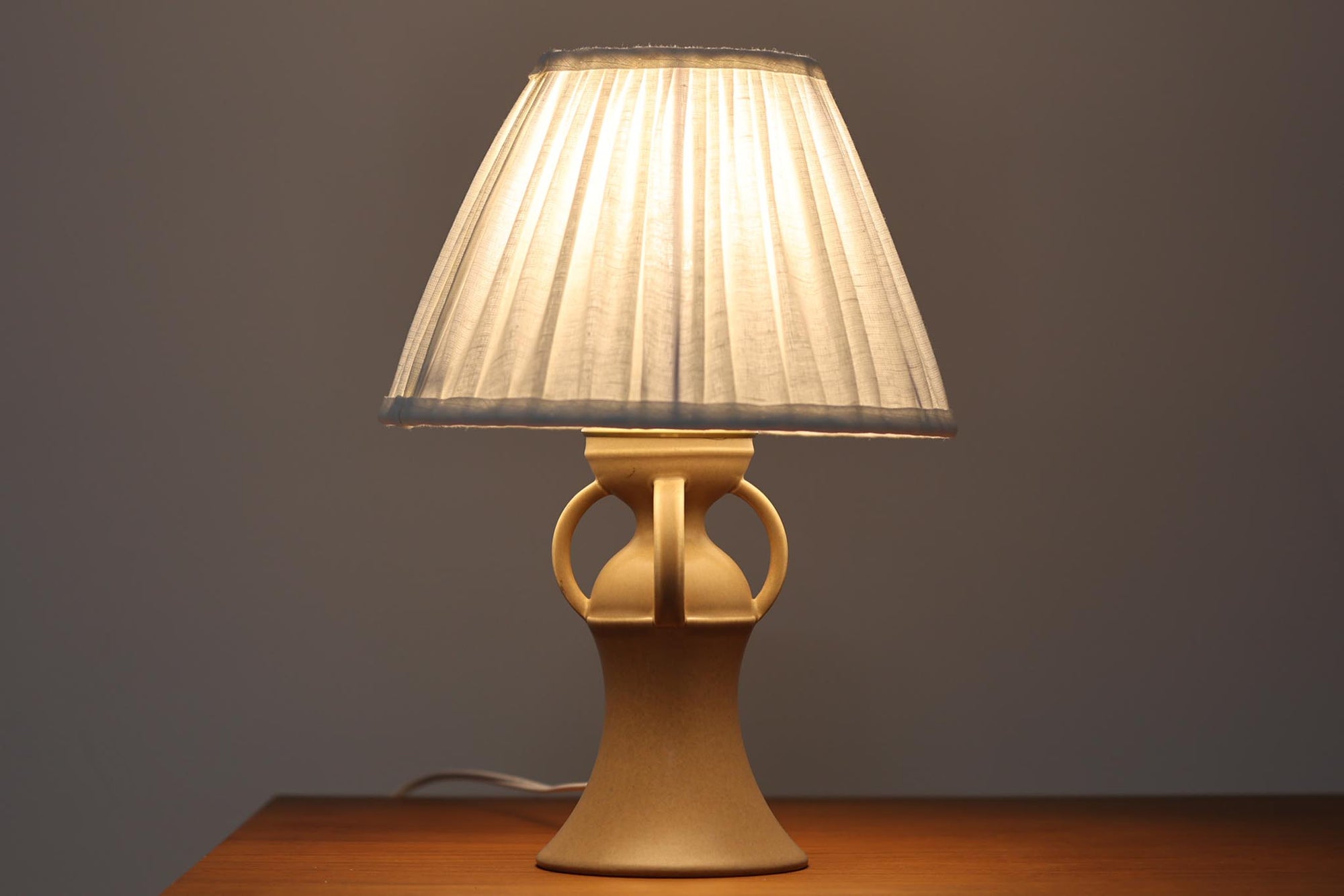 1993年にLe Klint創業50周年を記念して制作された、限定モデルのテーブルランプ「309」。ベースにはボーンホルム島の名門陶器工房Soholm（スーホルム）製のストーンウェアを採用し、シェードはLe Klint社製ではありませんが、新品のリネン製プリーツシェードを合わせており、クラシカルな佇まいと柔らかな光を演出します。北欧らしい温かみと洗練された存在感を持ち、ベッドサイドやリビングのアクセントとして取り入れやすい一灯です。ランプ底面には限定番号（No.0723）が刻まれており、コレクターズアイテムとしても価値ある一品です。