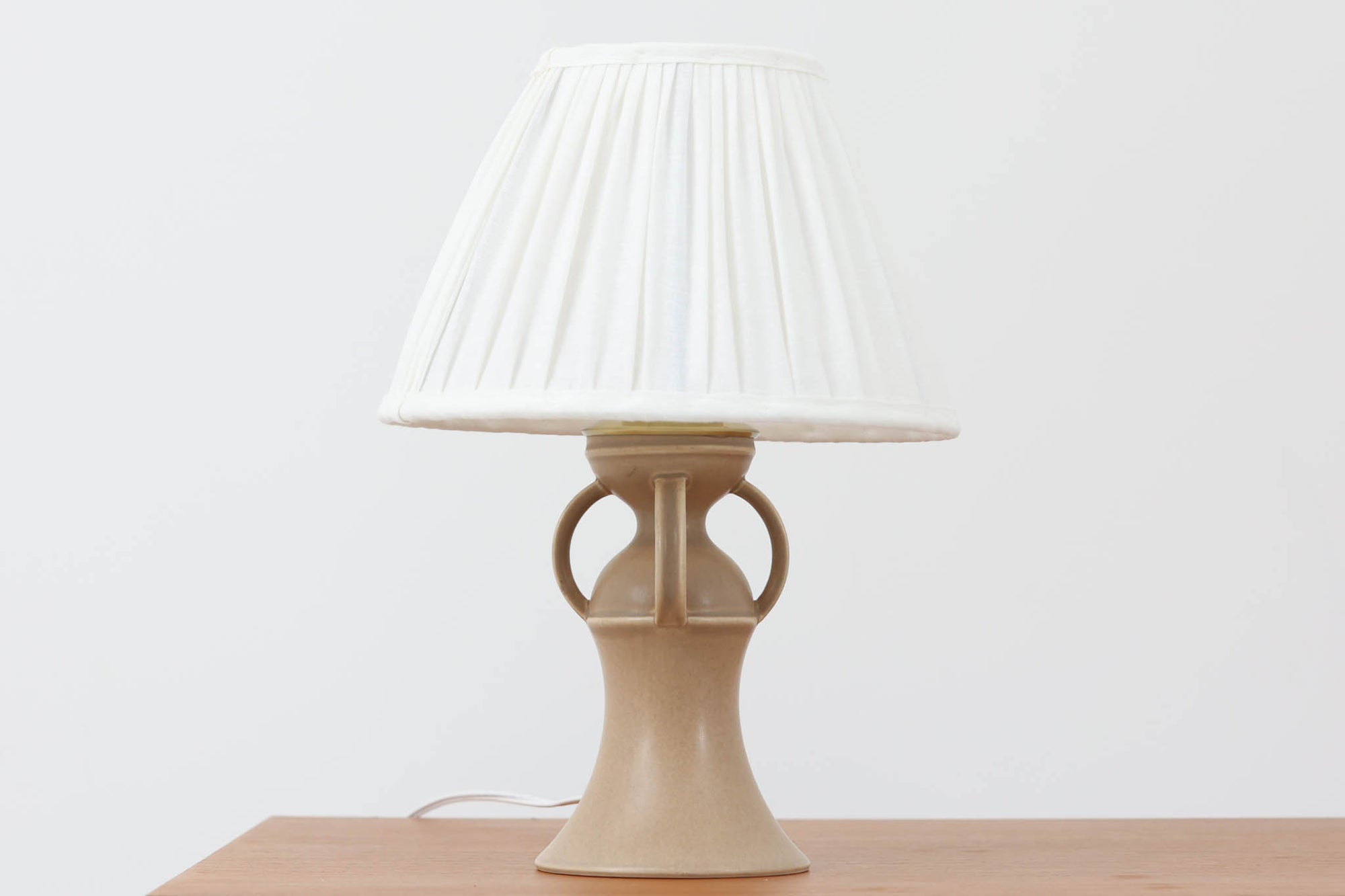 1993年にLe Klint創業50周年を記念して制作された、限定モデルのテーブルランプ「309」。ベースにはボーンホルム島の名門陶器工房Soholm（スーホルム）製のストーンウェアを採用し、シェードはLe Klint社製ではありませんが、新品のリネン製プリーツシェードを合わせており、クラシカルな佇まいと柔らかな光を演出します。北欧らしい温かみと洗練された存在感を持ち、ベッドサイドやリビングのアクセントとして取り入れやすい一灯です。ランプ底面には限定番号（No.0723）が刻まれており、コレクターズアイテムとしても価値ある一品です。