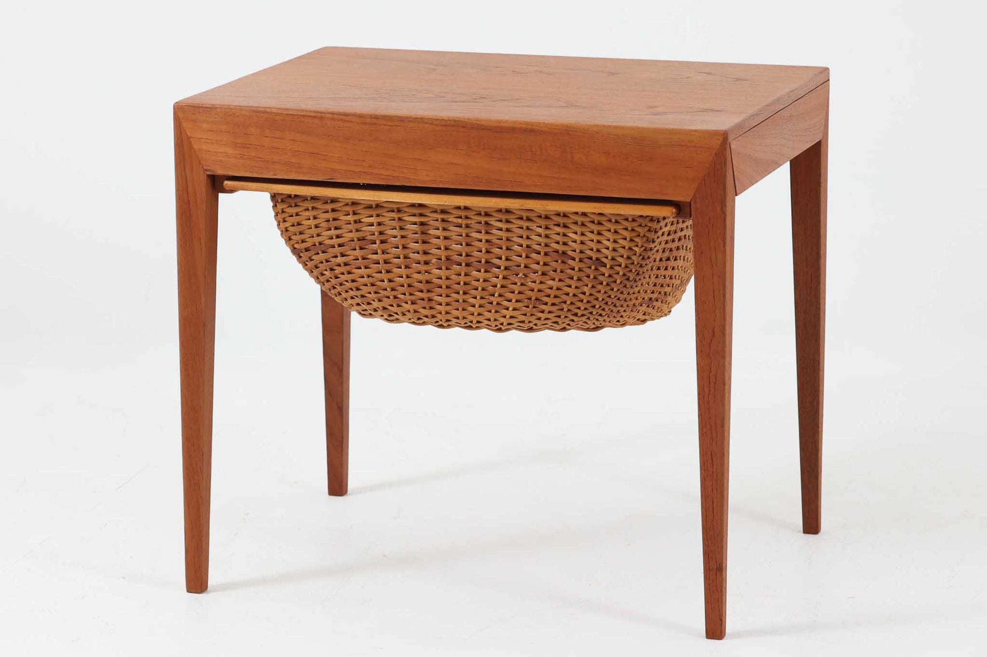デンマークの名デザイナーSeverin Hansen Jr.が手掛け、Haslev社によって製造された北欧ビンテージのソーイングテーブルです。素材には温かみのあるチーク材が使用され、シャープな接合部とすっきりとしたテーパードレッグが洗練された佇まいを演出しています。特徴的な籐のバスケットは糸や道具類をたっぷりと収納でき、天板下のスライドトレイには仕切りがあり細かな道具の整理にも便利です。バスケットを支える木製レールの一部に欠けがありますが、使用には支障ありません。実用性と美しさを兼ね備えた一台で、裁縫道具の収納にはもちろん、サイドテーブルとしてもおすすめです。