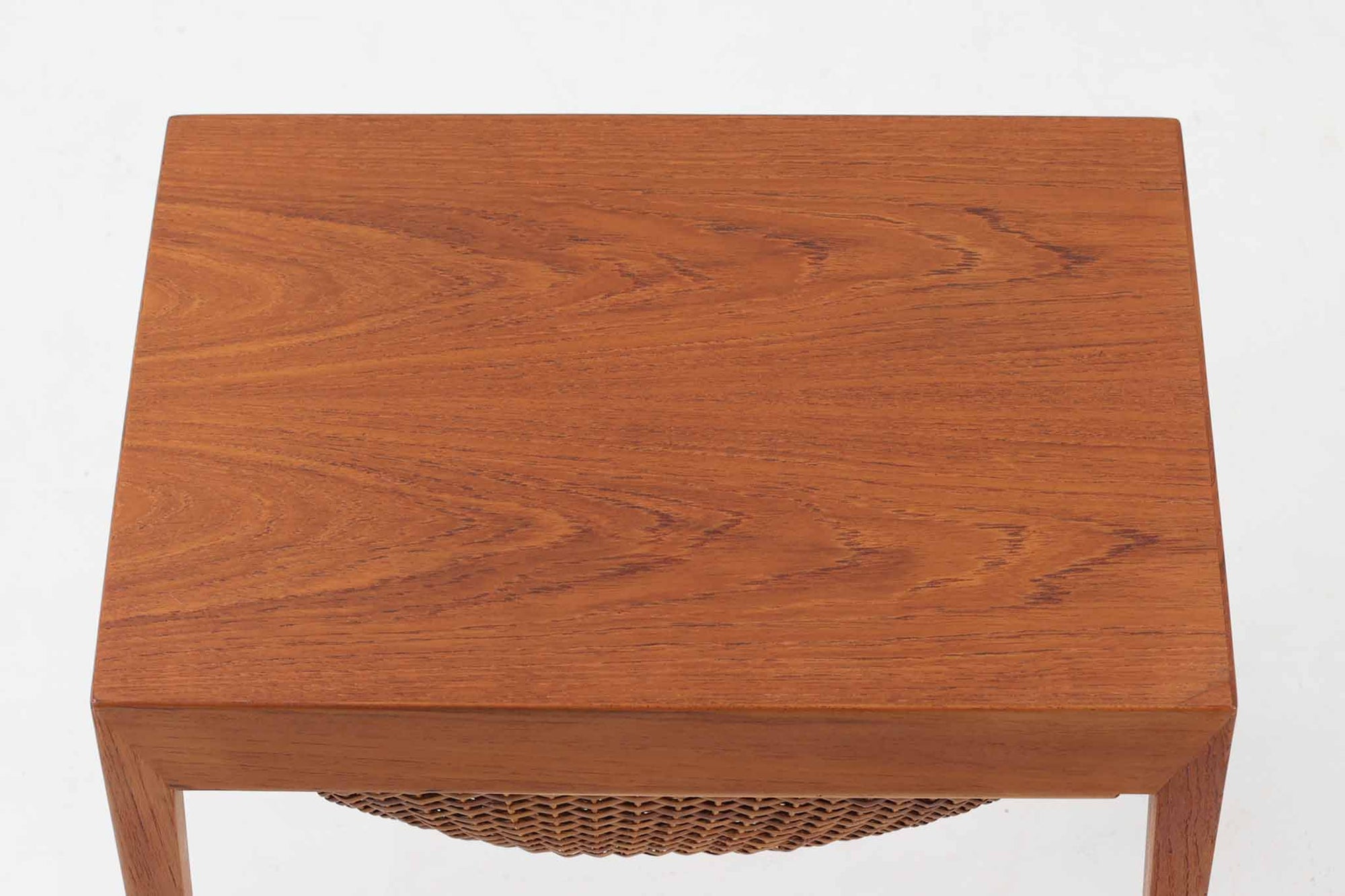 デンマークの名デザイナーSeverin Hansen Jr.が手掛け、Haslev社によって製造された北欧ビンテージのソーイングテーブルです。素材には温かみのあるチーク材が使用され、シャープな接合部とすっきりとしたテーパードレッグが洗練された佇まいを演出しています。特徴的な籐のバスケットは糸や道具類をたっぷりと収納でき、天板下のスライドトレイには仕切りがあり細かな道具の整理にも便利です。バスケットを支える木製レールの一部に欠けがありますが、使用には支障ありません。実用性と美しさを兼ね備えた一台で、裁縫道具の収納にはもちろん、サイドテーブルとしてもおすすめです。