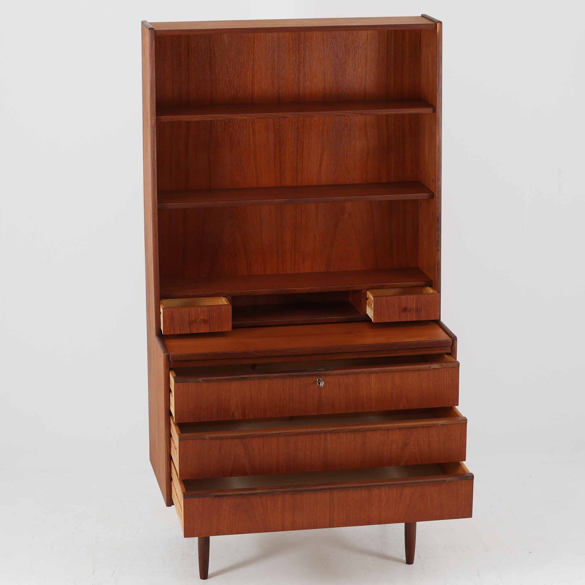 チーク材の温もりが魅力のこちらのディスプレイシェルフは、引き出し収納と棚が一体となった北欧ビンテージらしい実用性と美しさを兼ね備えた一台で、下段には鍵付きの3杯引き出し、上段には棚が3段設けられており、書斎やリビングの収納兼飾り棚としてはもちろん、店舗什器としても活躍します。細身の丸脚が全体に軽やかな印象を与え、チーク材特有の深みのある色合いと経年による艶が上質な雰囲気を醸し出しています。