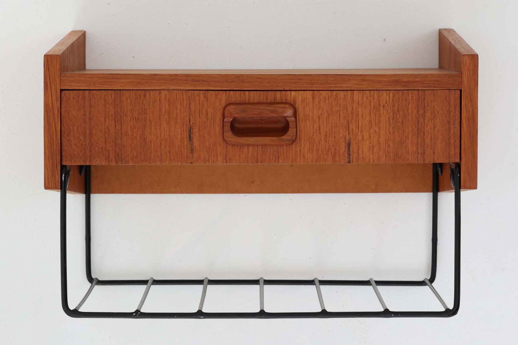 スウェーデン製のヴィンテージウォールシェルフ。温かみのあるチーク材と、ブラックスチールのコンビネーションが魅力的な一台です。シンプルな構成ながら、前面の丸みを帯びた掘り込み取手や、緩やかな角度のついたサイドパネルなど、北欧デザインらしい細やかなディテールが随所に見られます。引き出しには小物類をすっきりと収納でき、下部のスチールラックはマフラーや雑誌、スリッパなどの置き場としても便利。玄関やリビング、寝室など、さまざまな空間にフィットする汎用性の高いアイテムです。