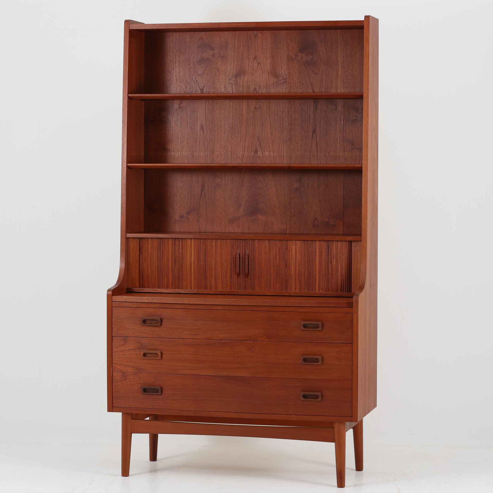 Johannes Sorth（ヨハネス・ソース）によるNexo Mobelfabrik社製のチーク材ディスプレイシェルフです。幅100cmと程よいサイズ感で、上段の棚は高さのある書籍やオブジェを飾るのに適しており、中央の蛇腹扉の内側には小引き出しや仕切りが備わり、細かな収納にも対応します。下段の3杯の引き出しは収納力に優れ、衣類や書類の整理に便利です。直線的なフォルムに温かみのあるチーク材の木目が映え、経年の艶が深みを増したビンテージらしい風合いを楽しめます。機能性と美観を兼ね備えた北欧家具の魅力が詰まった一台です。