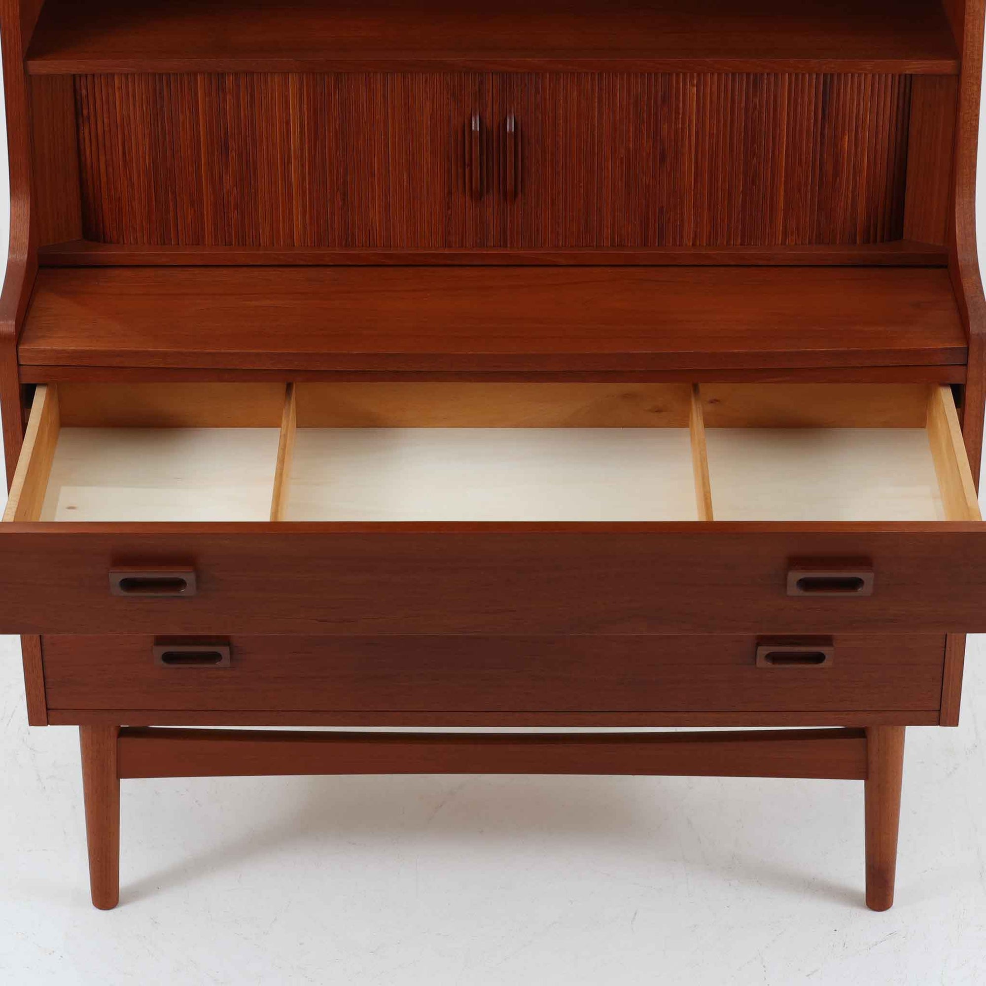 Johannes Sorth（ヨハネス・ソース）によるNexo Mobelfabrik社製のチーク材ディスプレイシェルフです。幅100cmと程よいサイズ感で、上段の棚は高さのある書籍やオブジェを飾るのに適しており、中央の蛇腹扉の内側には小引き出しや仕切りが備わり、細かな収納にも対応します。下段の3杯の引き出しは収納力に優れ、衣類や書類の整理に便利です。直線的なフォルムに温かみのあるチーク材の木目が映え、経年の艶が深みを増したビンテージらしい風合いを楽しめます。機能性と美観を兼ね備えた北欧家具の魅力が詰まった一台です。