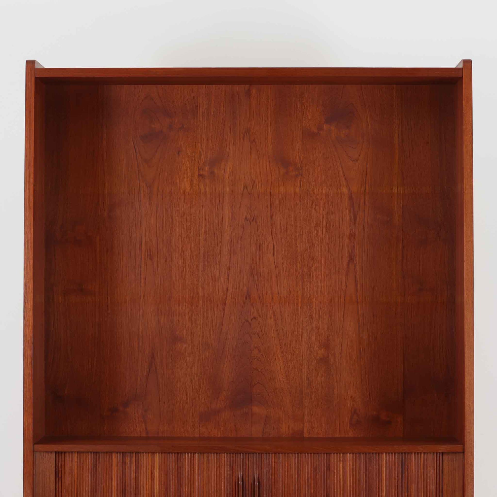 Johannes Sorth（ヨハネス・ソース）によるNexo Mobelfabrik社製のチーク材ディスプレイシェルフです。幅100cmと程よいサイズ感で、上段の棚は高さのある書籍やオブジェを飾るのに適しており、中央の蛇腹扉の内側には小引き出しや仕切りが備わり、細かな収納にも対応します。下段の3杯の引き出しは収納力に優れ、衣類や書類の整理に便利です。直線的なフォルムに温かみのあるチーク材の木目が映え、経年の艶が深みを増したビンテージらしい風合いを楽しめます。機能性と美観を兼ね備えた北欧家具の魅力が詰まった一台です。