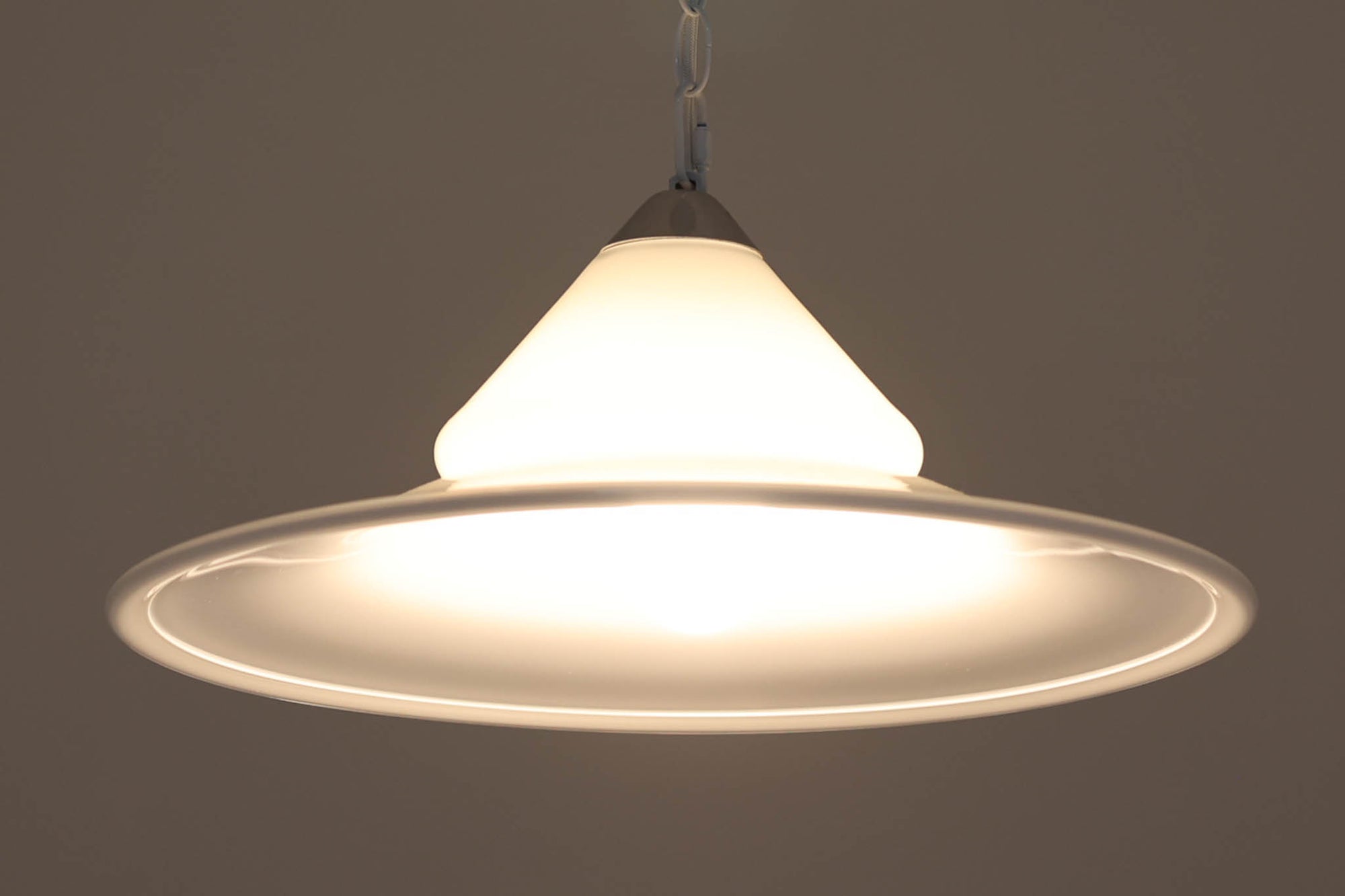 デンマークの名窯、Royal Copenhagen（ロイヤルコペンハーゲン）によるビンテージペンダントライト「Opus」。直径44cmのガラスシェードは、乳白色の滑らかな質感と優美な曲線を持ち、点灯時には柔らかな光をふんわりと拡散します。シェードの中央部にさりげない段差を設けたデザインは、シンプルながらも立体感があり、空間に洗練されたアクセントを加えます。金属パーツにはやや経年の使用感が見られますが、シェード自体は非常に良好な状態で、ガラスの透明感と清潔感を十分に感じられます。ダイニングやリビング、吹き抜けの空間など、幅広いインテリアにマッチし、北欧モダンな空間演出にぴったりの一灯です。