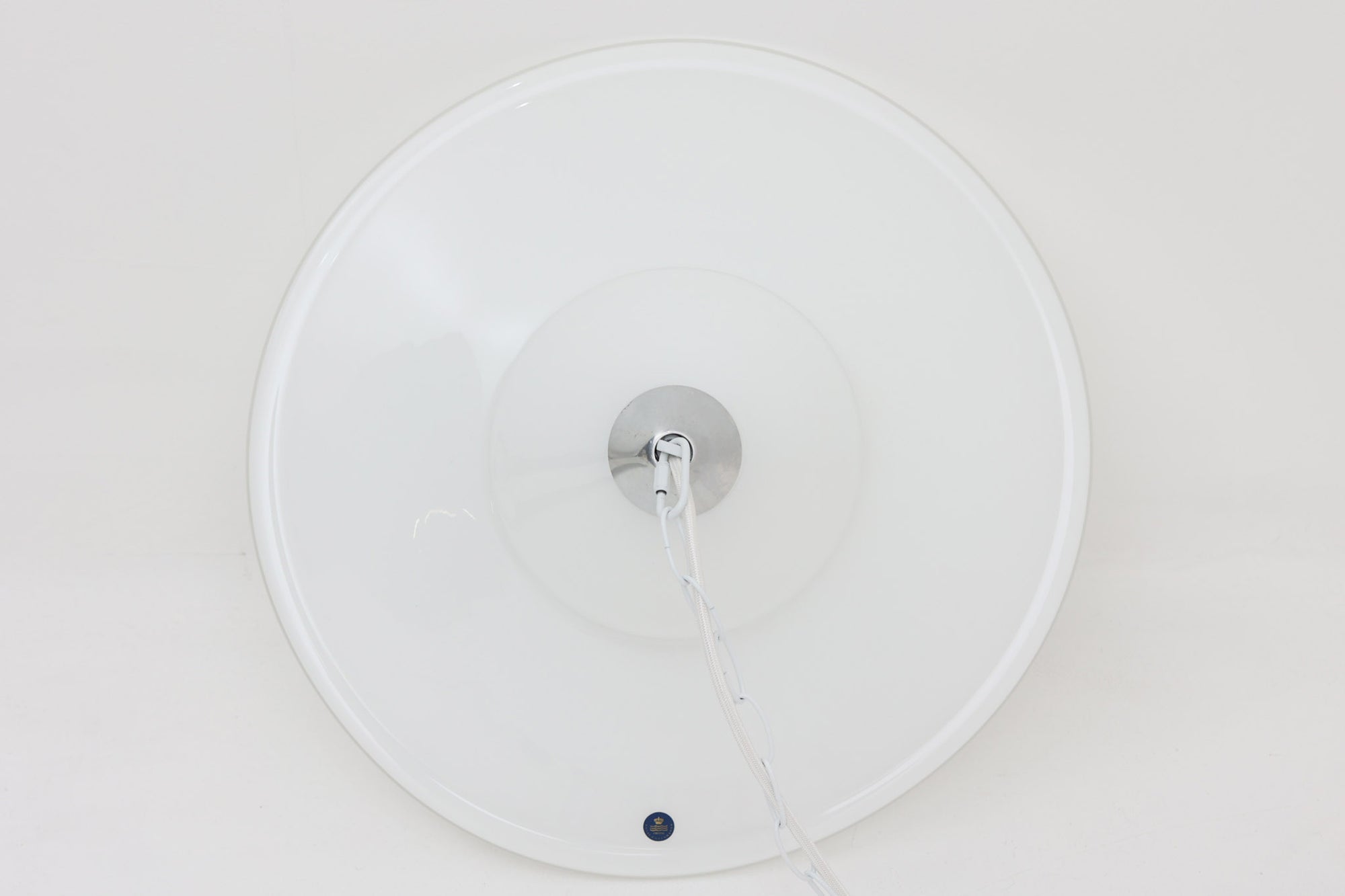 デンマークの名窯、Royal Copenhagen（ロイヤルコペンハーゲン）によるビンテージペンダントライト「Opus」。直径44cmのガラスシェードは、乳白色の滑らかな質感と優美な曲線を持ち、点灯時には柔らかな光をふんわりと拡散します。シェードの中央部にさりげない段差を設けたデザインは、シンプルながらも立体感があり、空間に洗練されたアクセントを加えます。金属パーツにはやや経年の使用感が見られますが、シェード自体は非常に良好な状態で、ガラスの透明感と清潔感を十分に感じられます。ダイニングやリビング、吹き抜けの空間など、幅広いインテリアにマッチし、北欧モダンな空間演出にぴったりの一灯です。