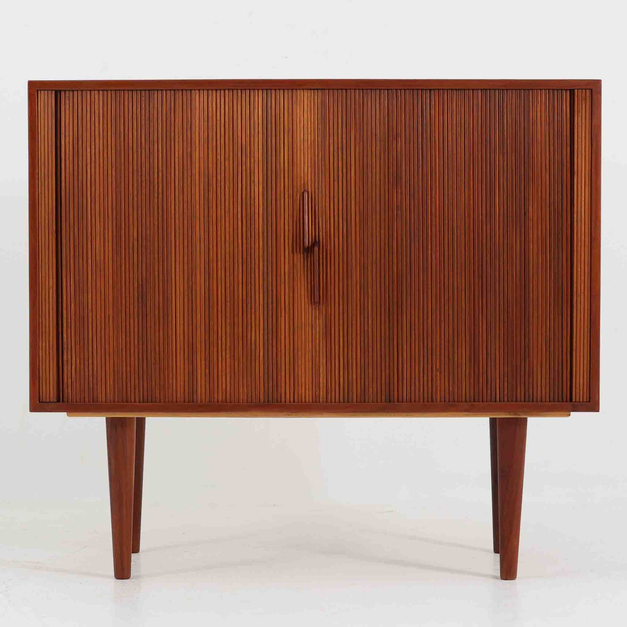Kai Kristiansen（カイ・クリスチャンセン）によるデザインで、Feldballes Mobelfabrik社から製造された蛇腹キャビネットです。繊細なスリットが並ぶチーク材のロールフロントは職人技が光る美しい仕上がりで、滑らかな開閉動作も魅力のひとつ。内部は仕切り板と小収納が備えられ、実用性にも優れています。右下の小収納部は前板のみが貼られた飾り構造で、内部に収納はありません。特注仕様と思われる希少な一点です。シンプルながら存在感があり、リビングやワークスペースにも調和する北欧ビンテージらしい端正な佇まいです。