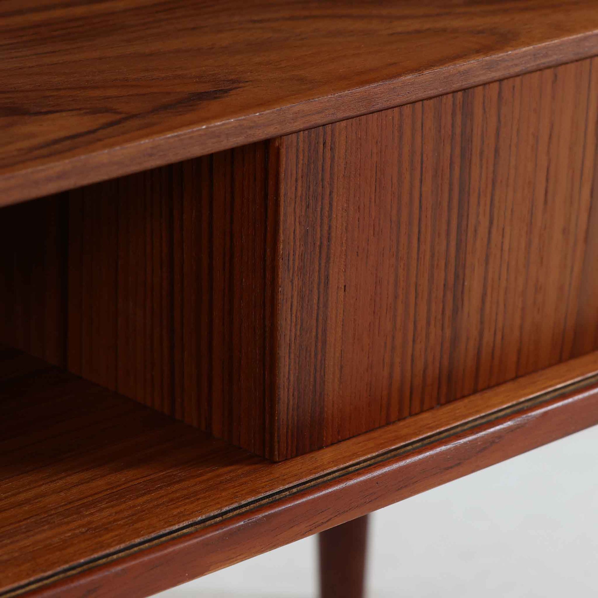 Kai Kristiansen（カイ・クリスチャンセン）によるデザインで、Feldballes Mobelfabrik社から製造された蛇腹キャビネットです。繊細なスリットが並ぶチーク材のロールフロントは職人技が光る美しい仕上がりで、滑らかな開閉動作も魅力のひとつ。内部は仕切り板と小収納が備えられ、実用性にも優れています。右下の小収納部は前板のみが貼られた飾り構造で、内部に収納はありません。特注仕様と思われる希少な一点です。シンプルながら存在感があり、リビングやワークスペースにも調和する北欧ビンテージらしい端正な佇まいです。