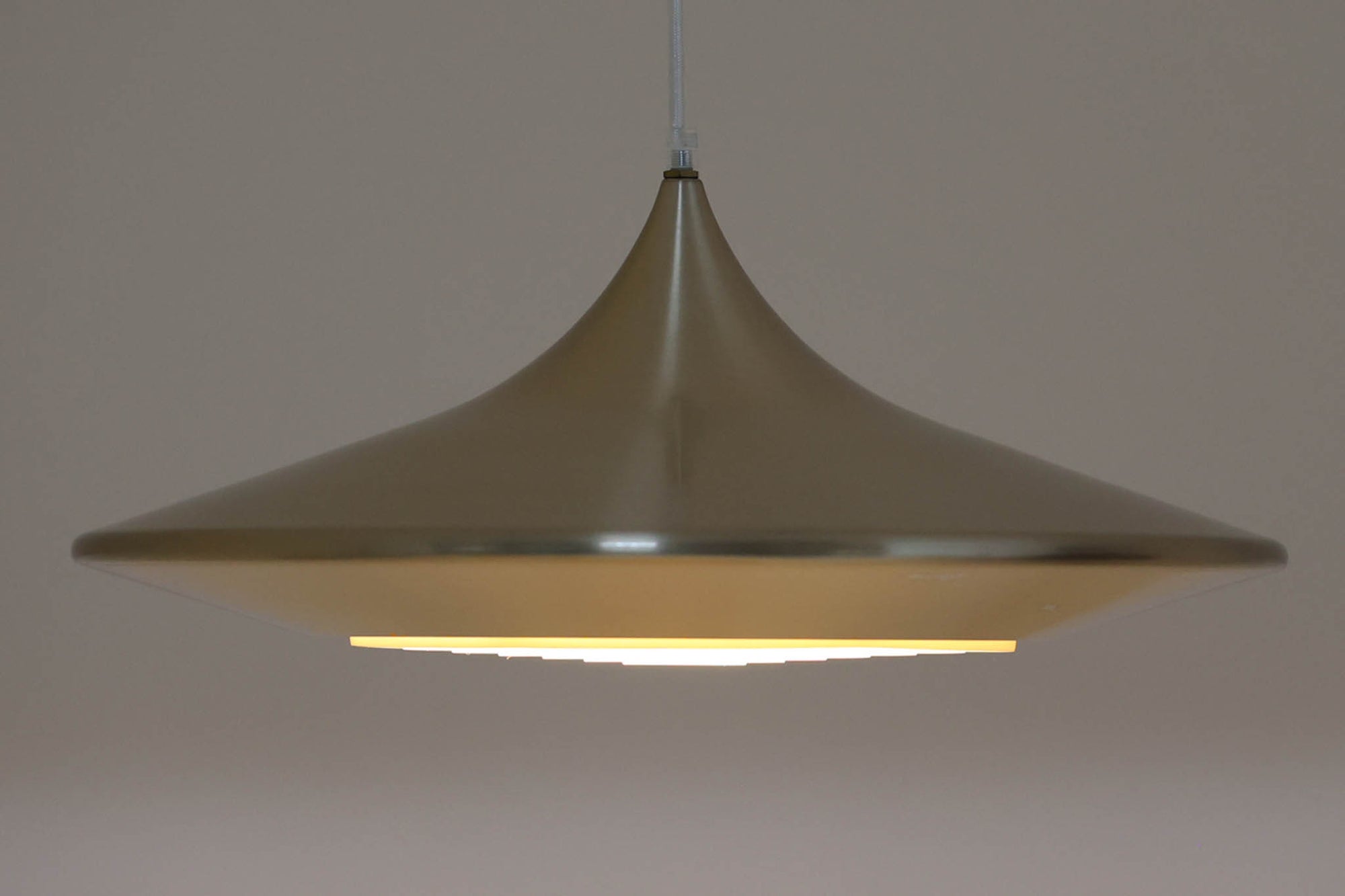 デンマークの照明メーカーLyfa社による、デザイナーEjnar B. mielby（アイナー・B・ミェルビー）が手がけた「Kuli（クーリ）」ペンダントライト。特徴的なホーン型のフォルムと、美しく仕上げられた真鍮カラーのシェードが印象的なビンテージ照明です。直径49cmと存在感のあるサイズ感で、ダイニングテーブルの上などにおすすめです。下面にはグリッド状のルーバーが備わっており、光源を柔らかく拡散しつつ眩しさを軽減する構造となっています。ソケット部分はE26口金、コードは引っ掛けシーリング仕様で、設置も簡単です。経年に伴う小傷や塗装剥がれが一部見られますが、全体としてはビンテージらしい雰囲気を保っています。空間にミッドセンチュリーのエッセンスを加える一品としておすすめです。