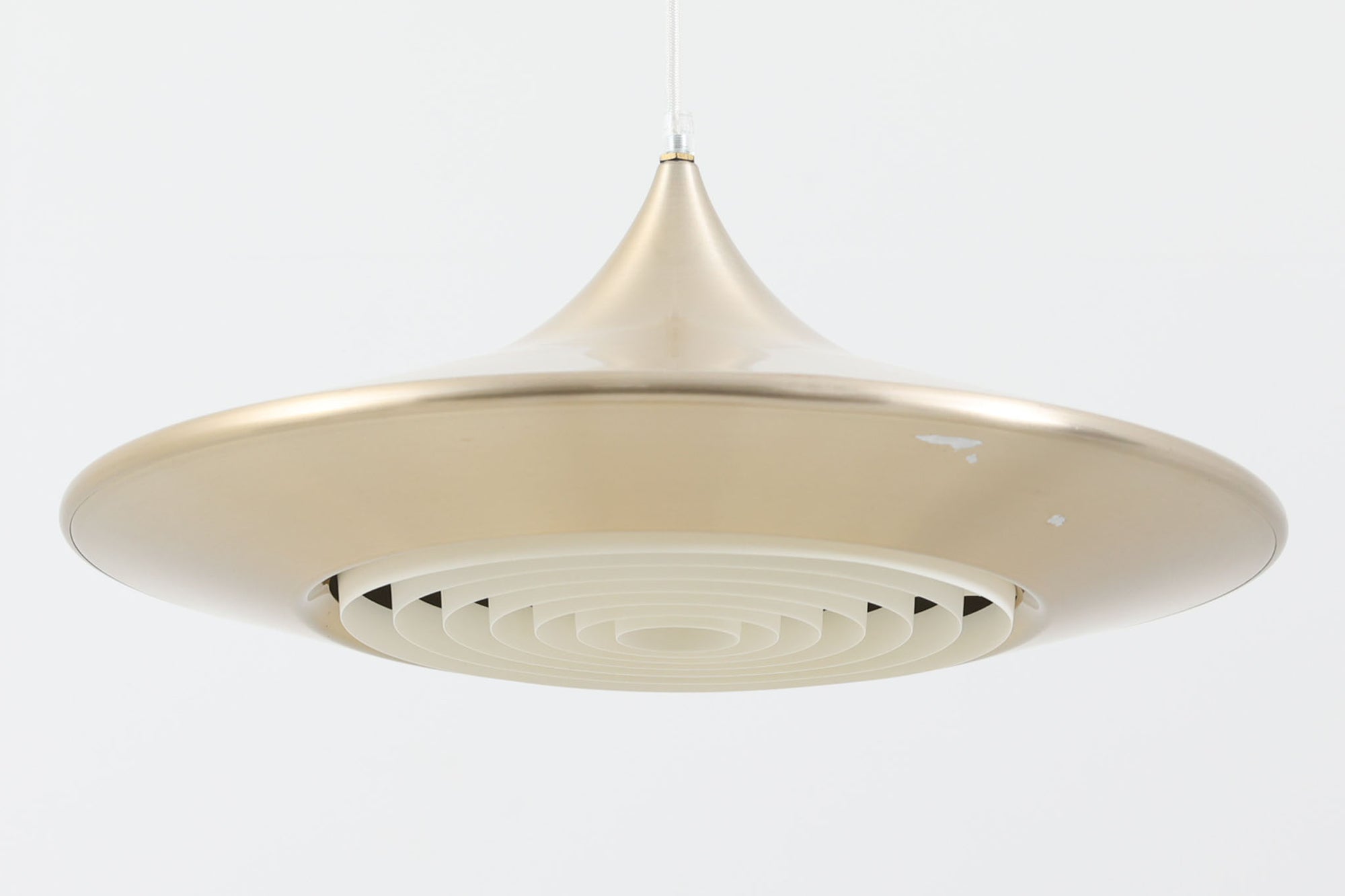 デンマークの照明メーカーLyfa社による、デザイナーEjnar B. mielby（アイナー・B・ミェルビー）が手がけた「Kuli（クーリ）」ペンダントライト。特徴的なホーン型のフォルムと、美しく仕上げられた真鍮カラーのシェードが印象的なビンテージ照明です。直径49cmと存在感のあるサイズ感で、ダイニングテーブルの上などにおすすめです。下面にはグリッド状のルーバーが備わっており、光源を柔らかく拡散しつつ眩しさを軽減する構造となっています。ソケット部分はE26口金、コードは引っ掛けシーリング仕様で、設置も簡単です。経年に伴う小傷や塗装剥がれが一部見られますが、全体としてはビンテージらしい雰囲気を保っています。空間にミッドセンチュリーのエッセンスを加える一品としておすすめです。